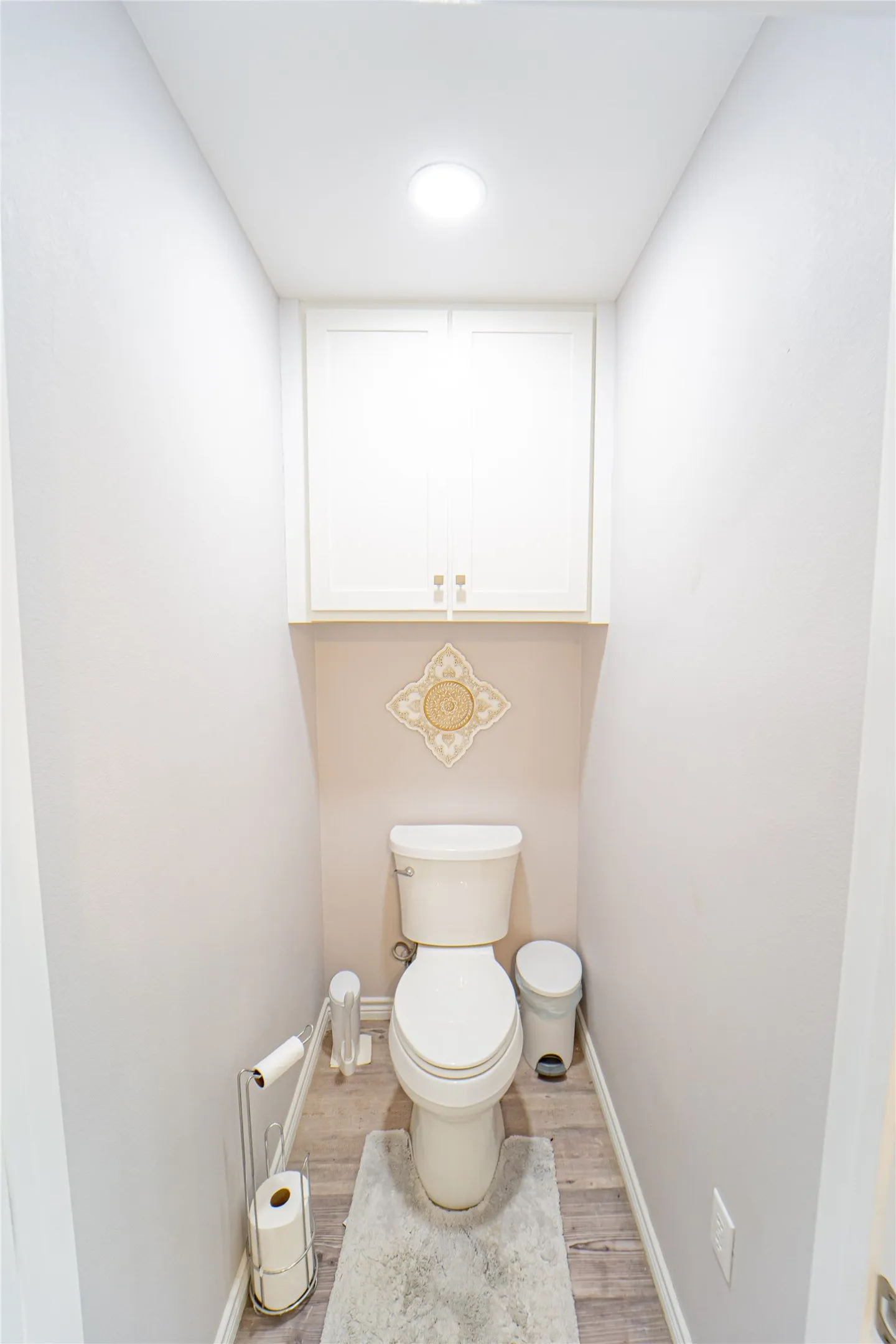 Powder room featuring light wood-finish flooring, white walls, and a built-in overhead cabinet with white shaker-style doors
