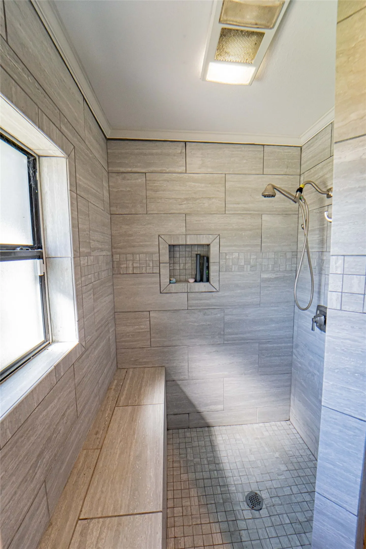 Tiled shower stall featuring a built-in bench, recessed niche, window, and square floor tiles