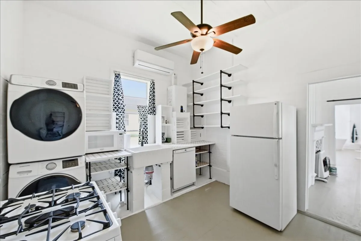 Kitchen/laundry area featuring stacked washer and dryer, white refrigerator, ceiling fan, and open storage shelves.
