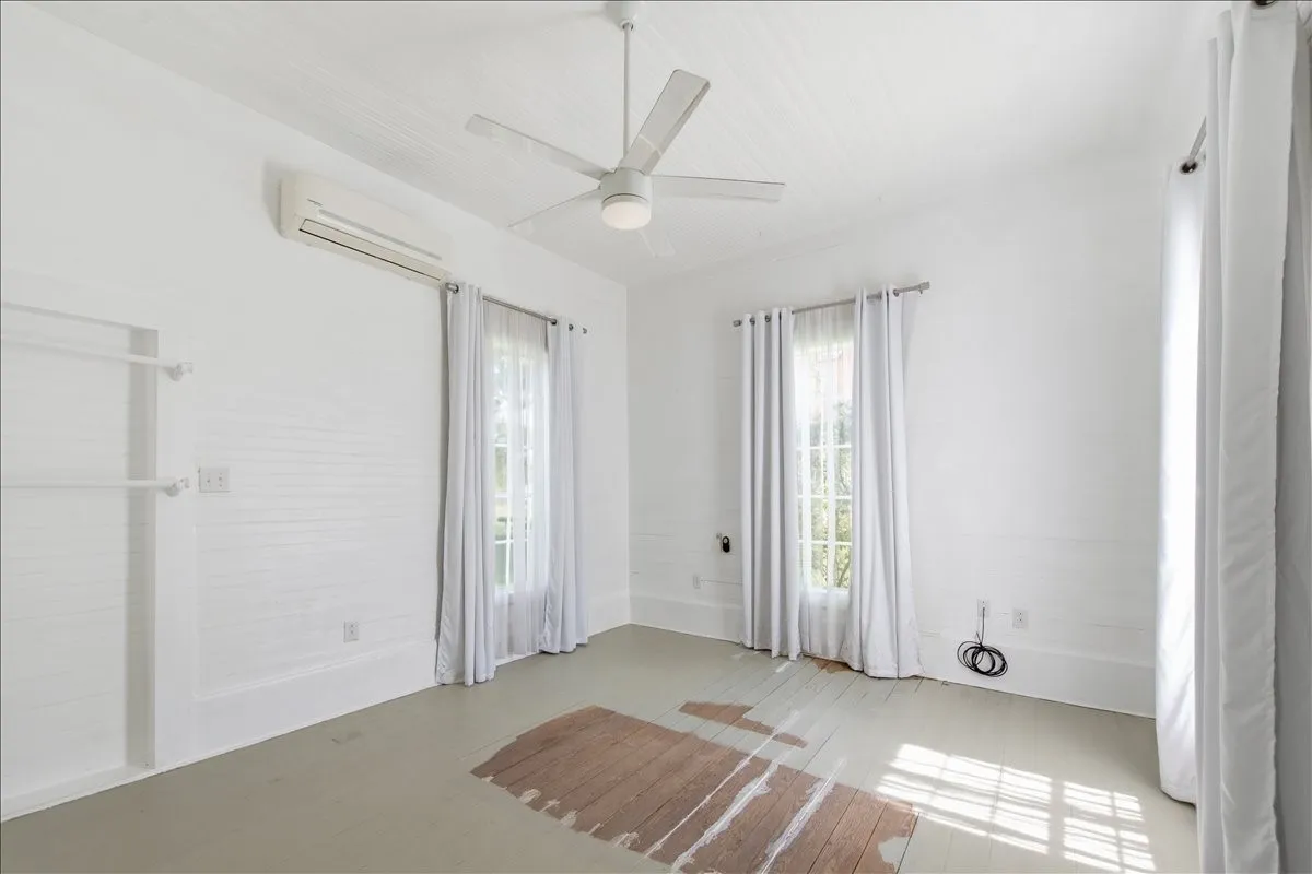 Airy interior room with high ceilings, ceiling fan, white paneled walls, and tall curtained windows.