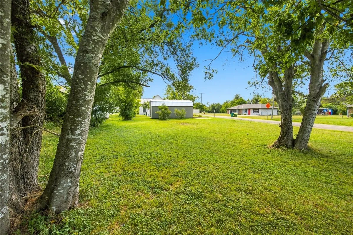 Shaded front yard area with expansive green lawn, mature trees, and a clear view across the property.