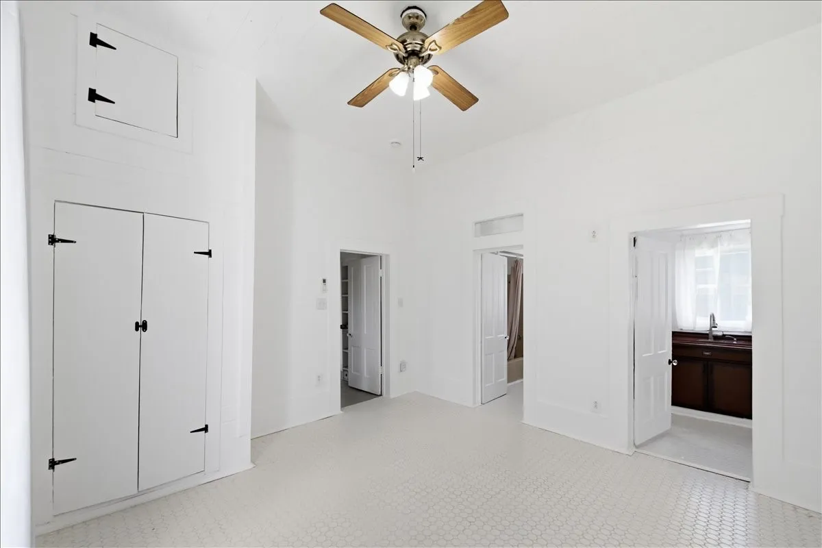Bright interior room featuring built-in white cabinetry, high ceilings, ceiling fan, and open doorways.