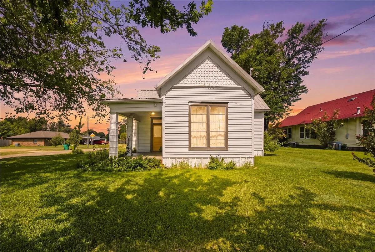 Twilight exterior shot showing warm interior lights glowing through the cottage windows against a colorful sky.