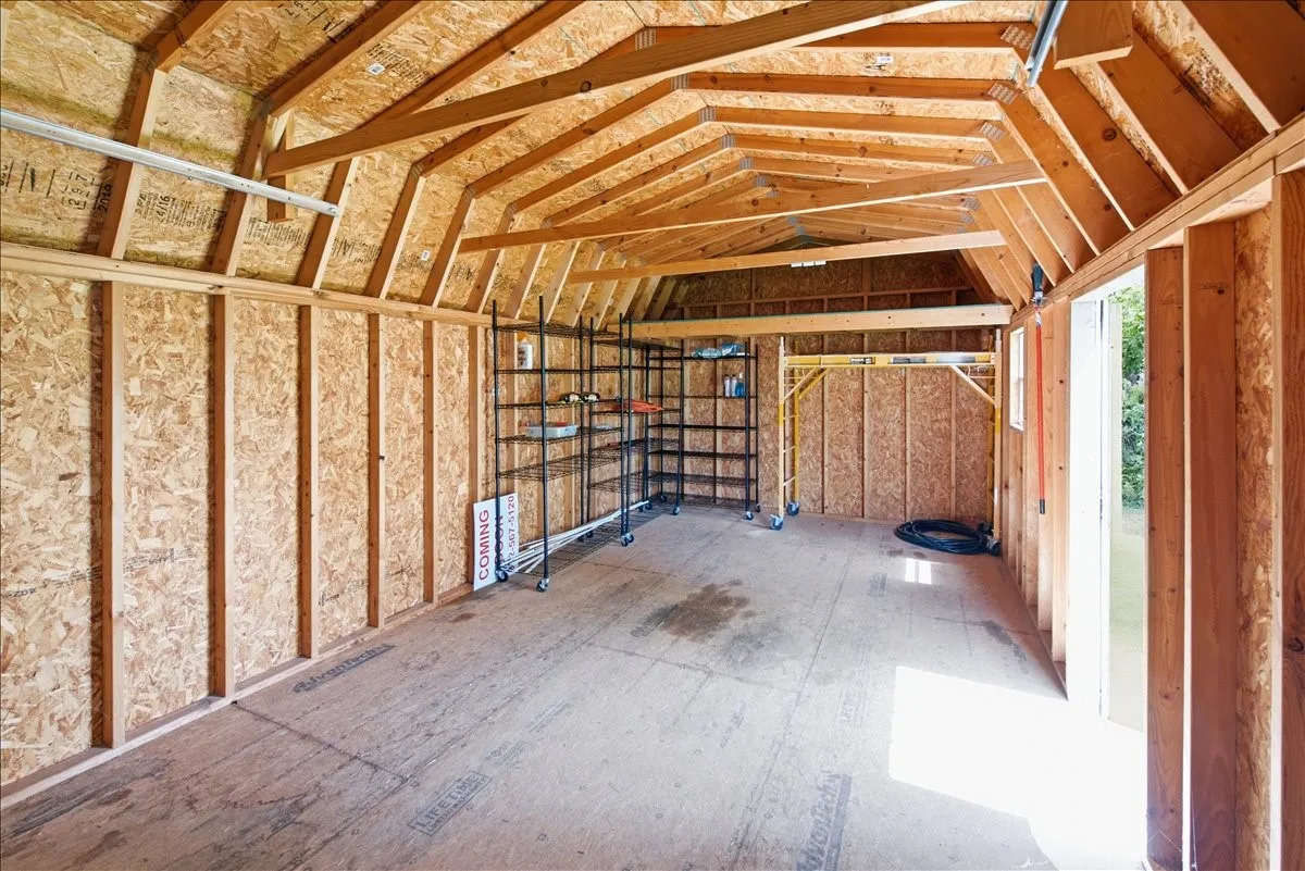Unfinished interior of the storage shed showing exposed wood framing, high ceilings, and concrete floor.