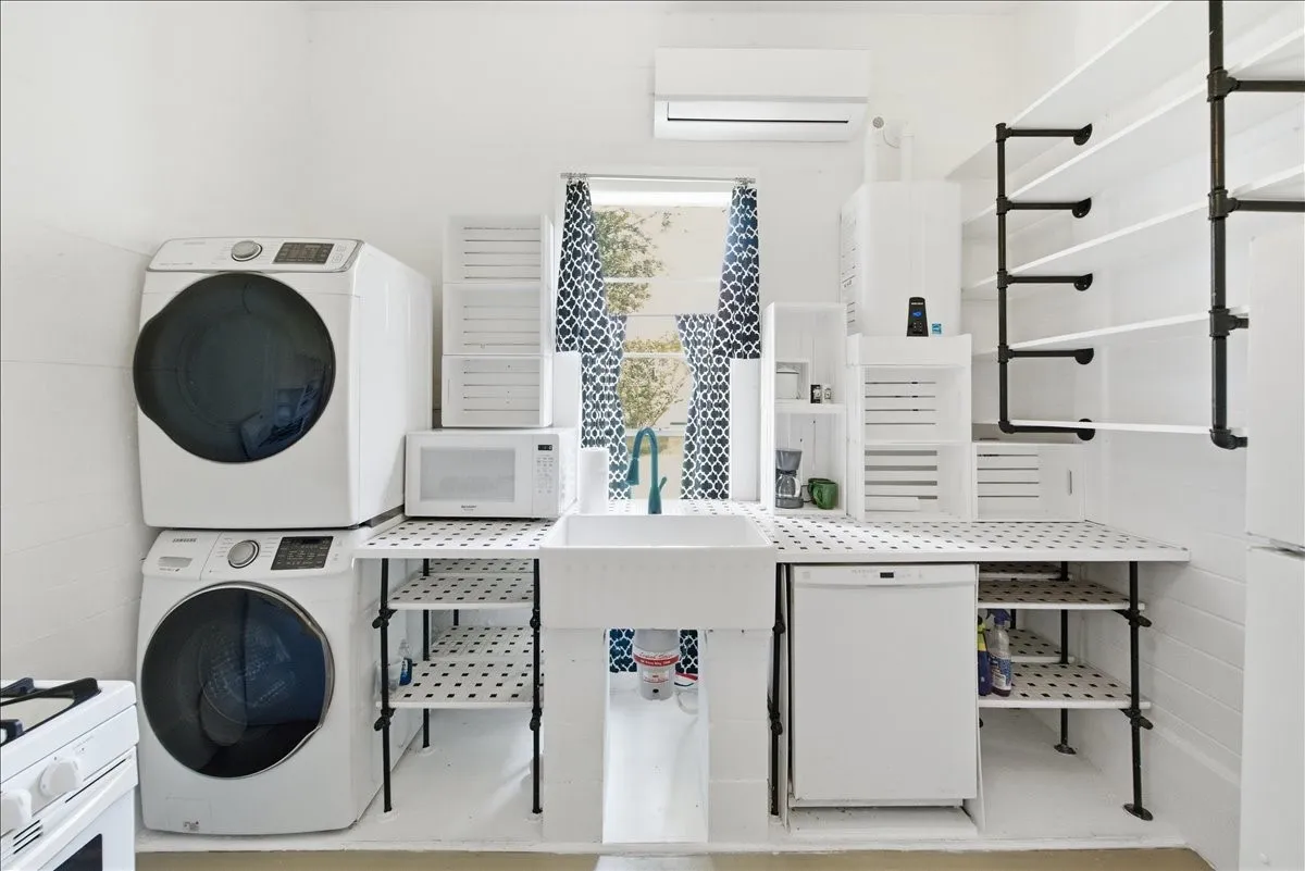 Utility room highlighting stacked washer and dryer unit, sink counter area, and open shelving storage.