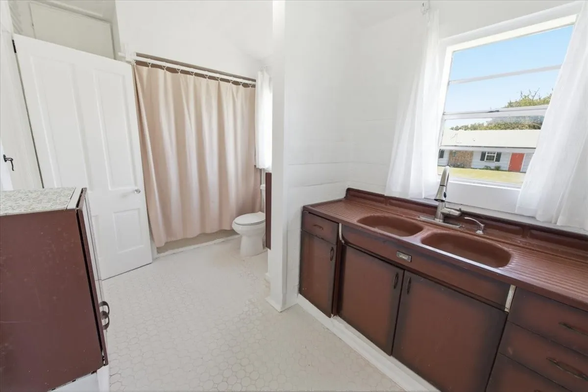 Bathroom view with double sink vanity, shower curtain, white walls, and a window for natural light.