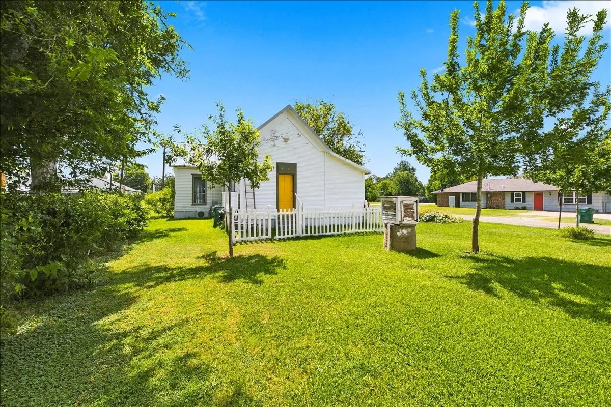 Wide yard view featuring young trees, a white cottage in the background, and open green space.