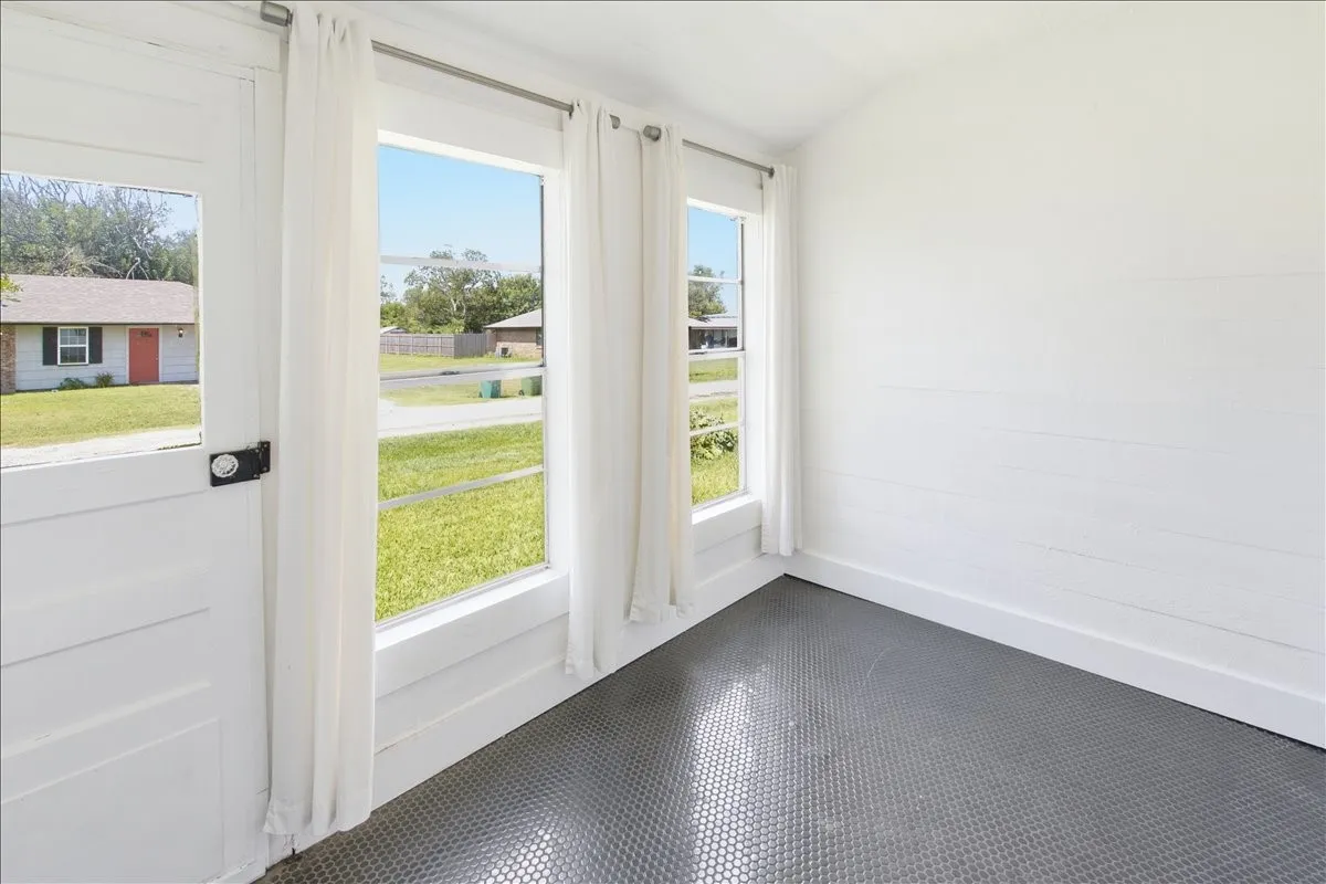 Sunlit interior hallway or porch nook with large windows overlooking the green outdoors.