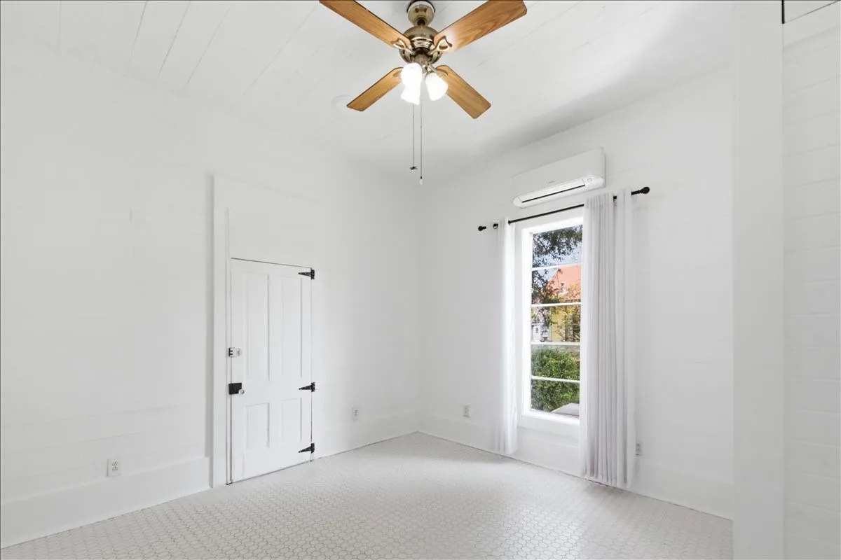 Clean white entryway/room featuring a ceiling fan, light fixture, and tall window with outdoor views.
