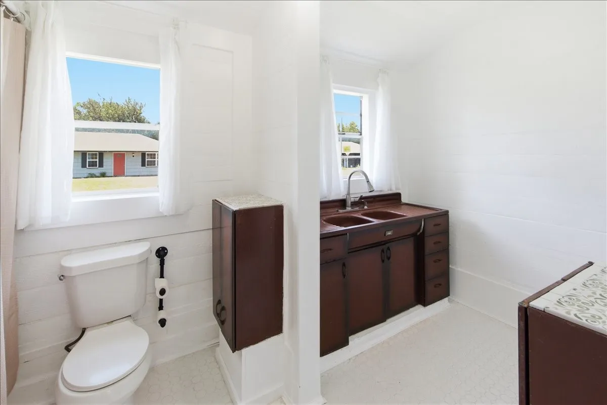 Alternate bathroom angle showing the toilet, dark wood double vanity, and window overlooking the property.