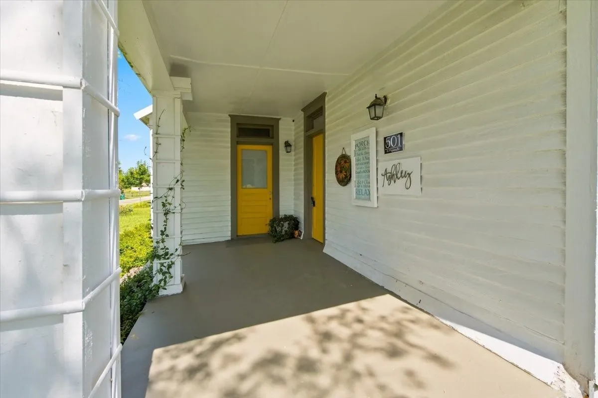 Covered front porch area with white siding, yellow front door, and views looking out toward the yard.
