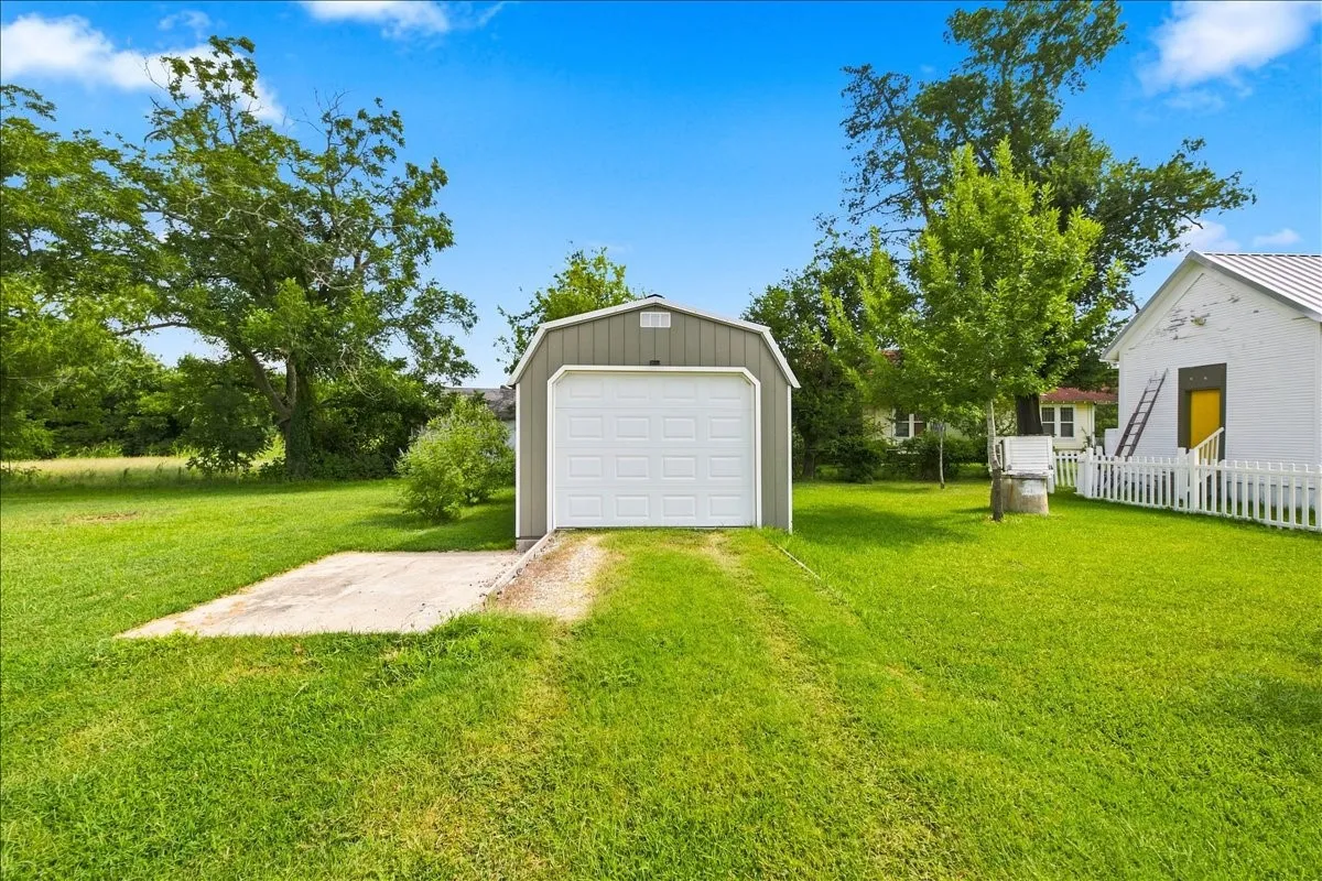 Detached shed or outbuilding set back on the sprawling green lawn under open blue skies.