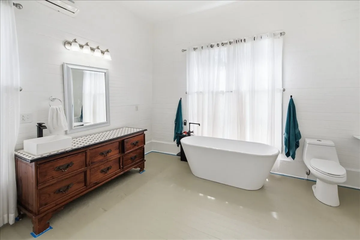 Alternate bathroom angle showing the dark wood vanity with mirror, freestanding tub, and bright white walls.