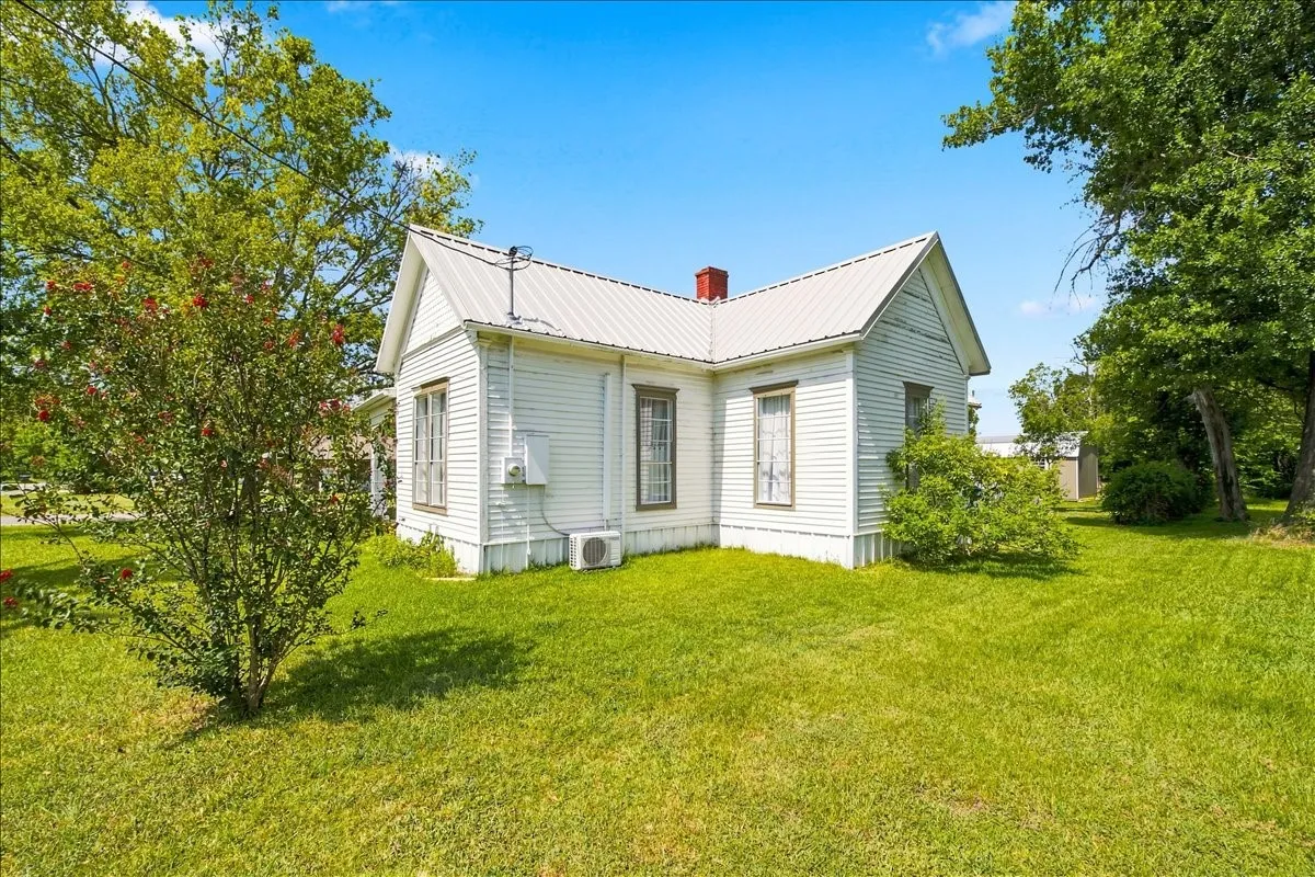 Full front view of the white cottage structure set on a wide, sunny grassy lot.