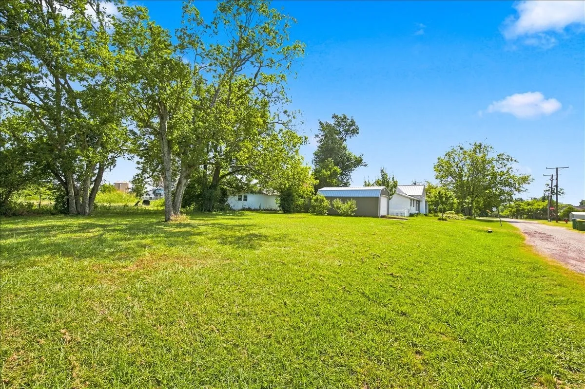 Spacious grassy front lawn featuring mature shade trees and a distant view of the cottage home.