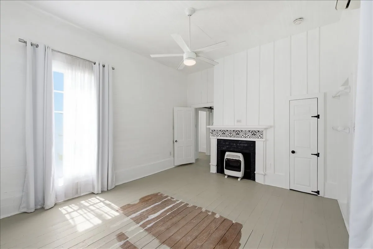 Living room view showcasing a decorative fireplace feature, ceiling fan, and large windows offering natural light.