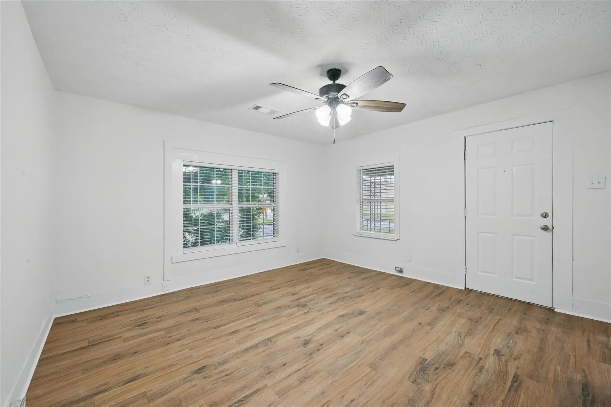 Empty room with light wood finished floors, a textured ceiling, and ceiling fan