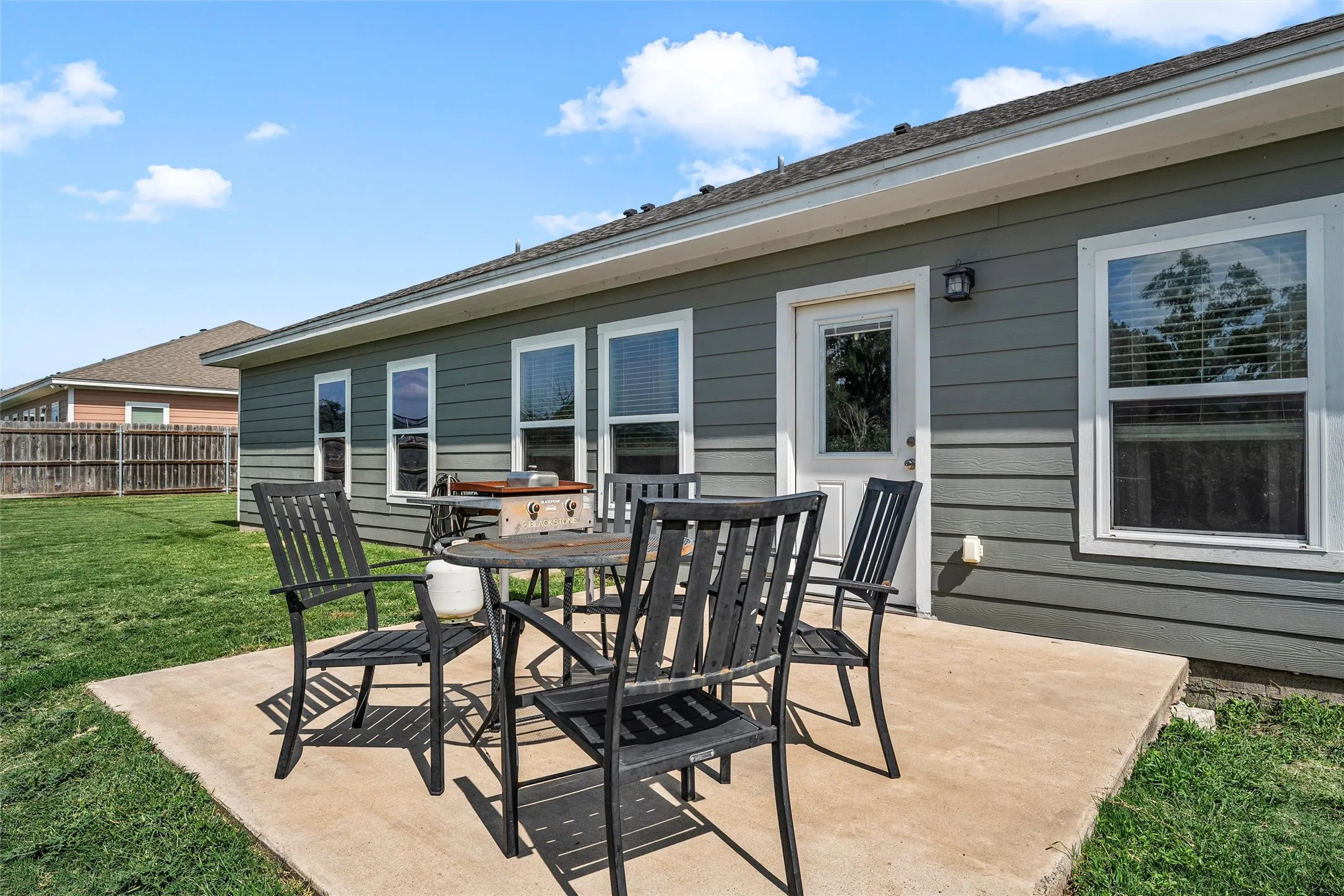Rear exterior featuring a concrete patio, a white paneled door, and multiple windows with white trim