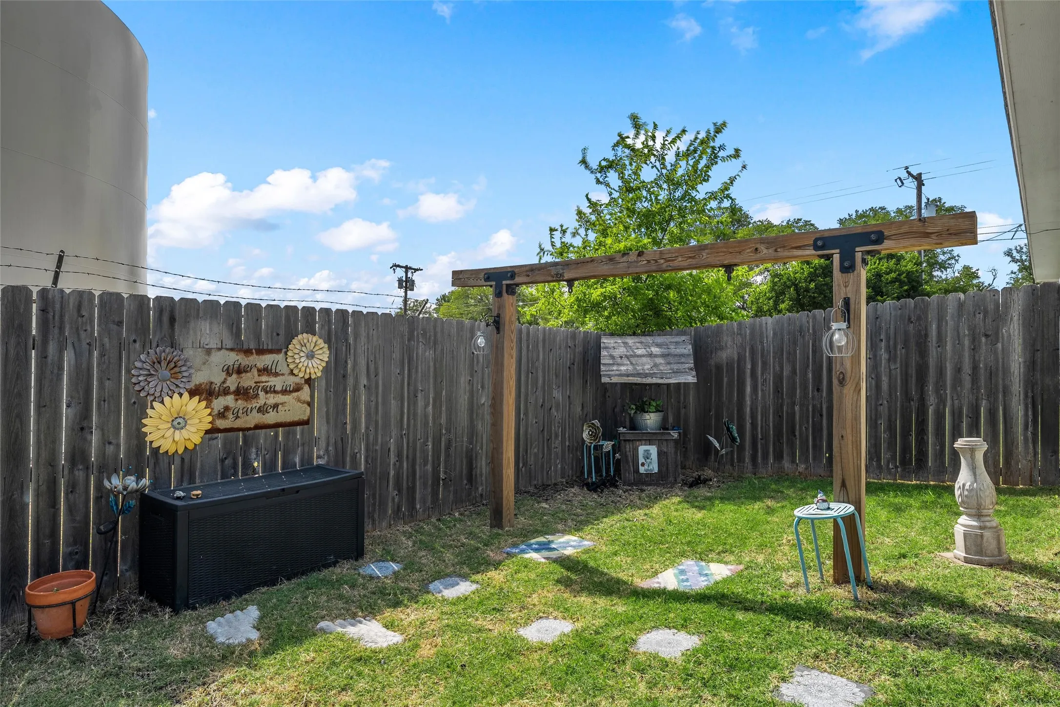 Private outdoor space featuring a full wood fence, a suspended wood beam structure, and stone pavers