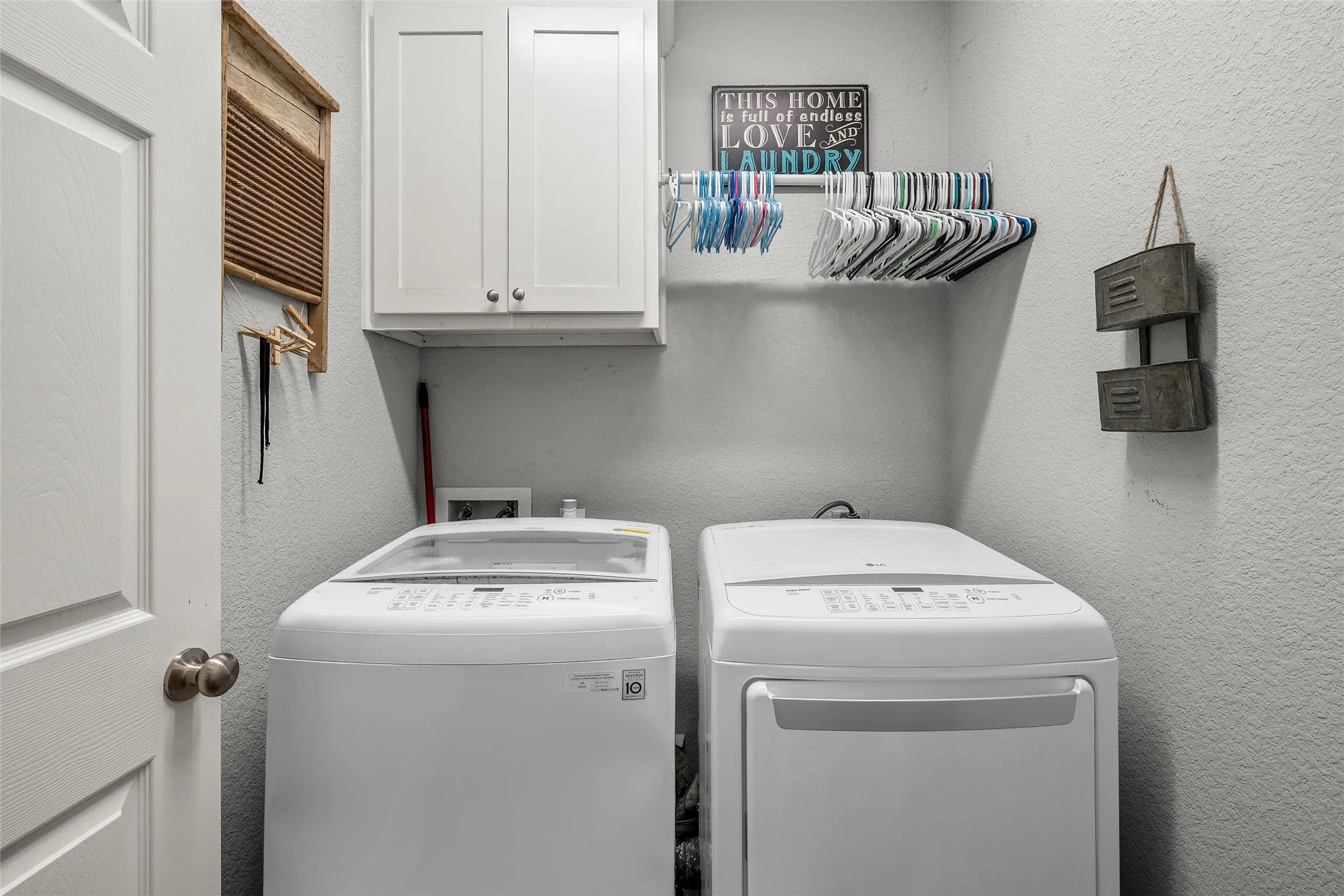 Laundry area with overhead white cabinetry, a built-in hanging rod, and textured walls