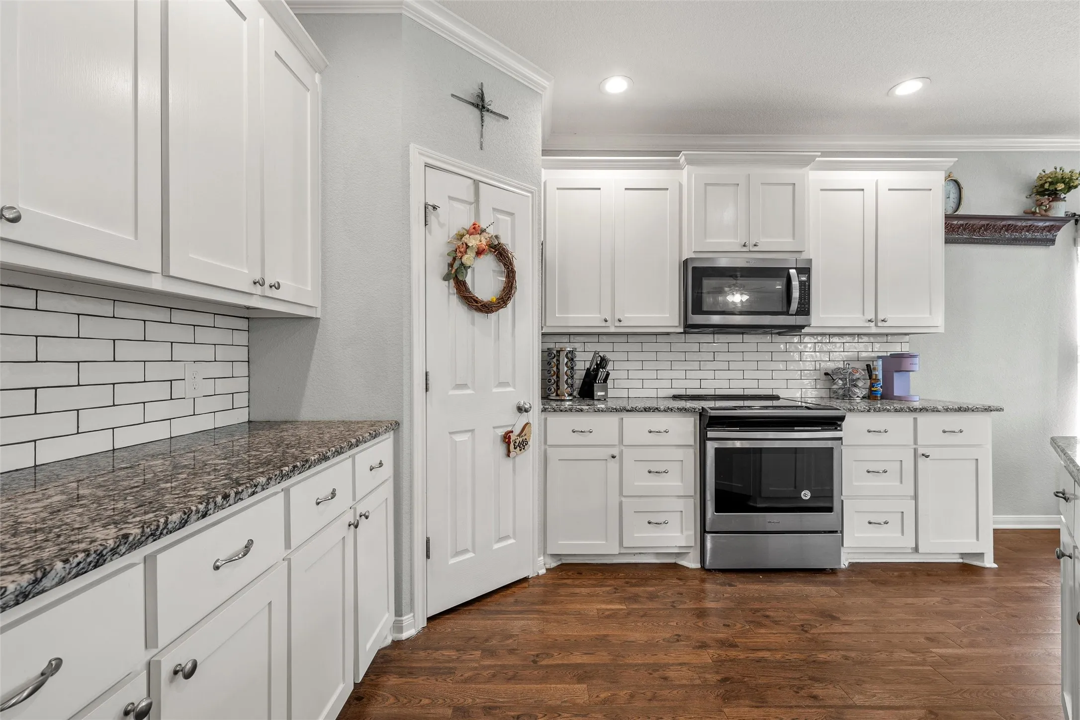 Kitchen featuring white shaker cabinetry, granite-style countertops, subway tile backsplash, stainless steel appliances, and wood-finish flooring