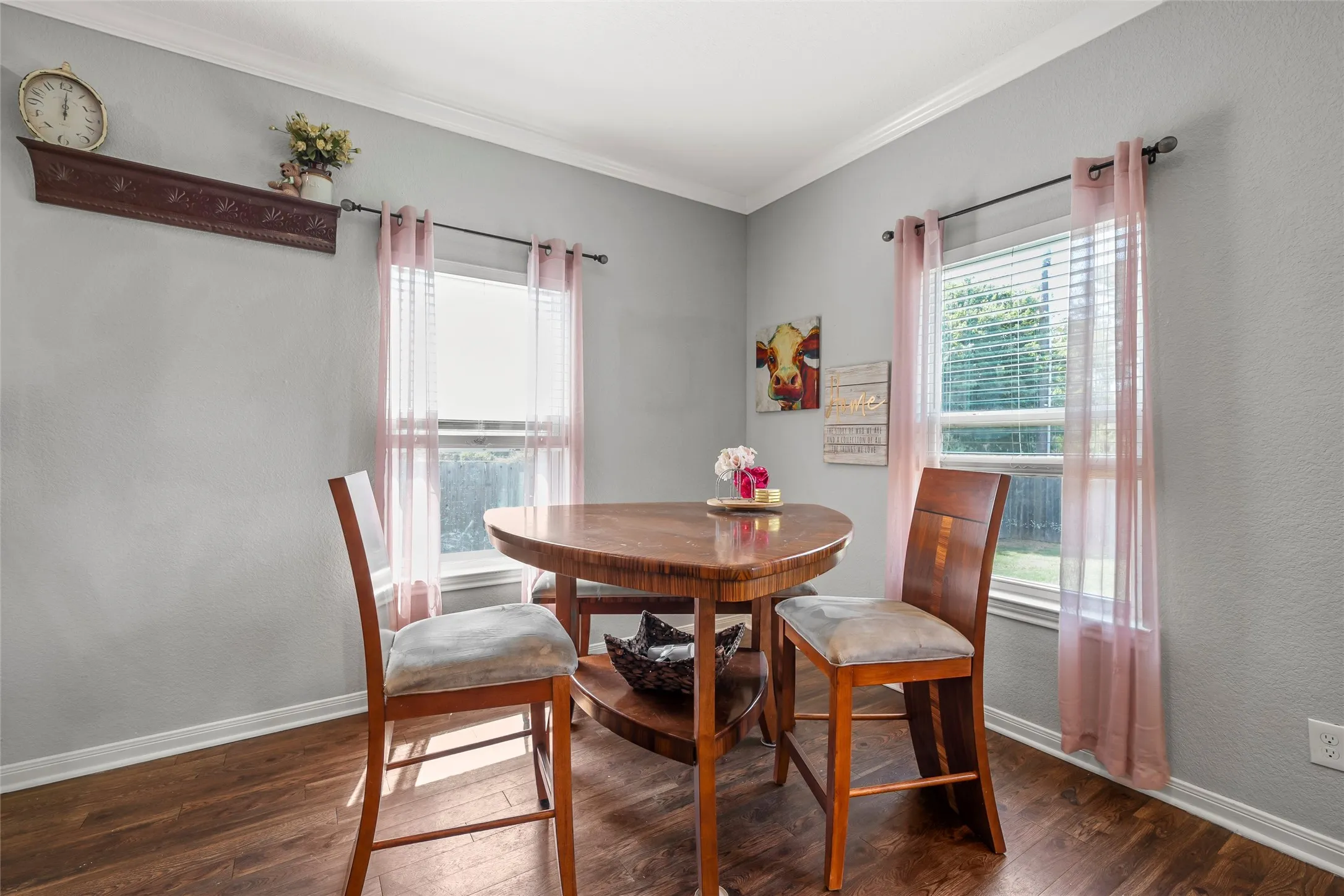 Dining area featuring wood-finish flooring, two windows with blinds, light gray wall paint, white crown molding, and white baseboards