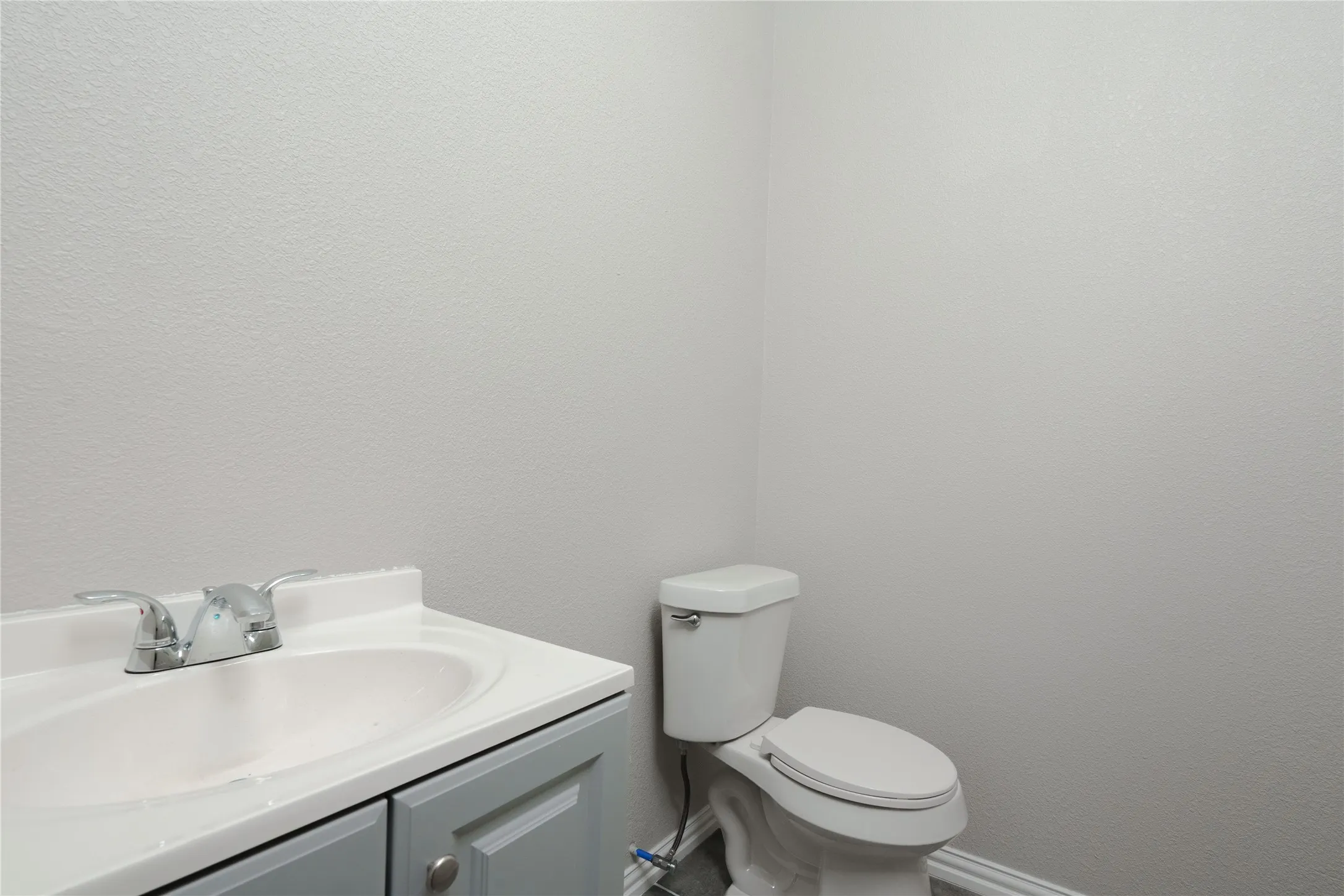 Bathroom featuring a white integrated sink, chrome faucet, gray vanity with cabinet storage, and a white toilet