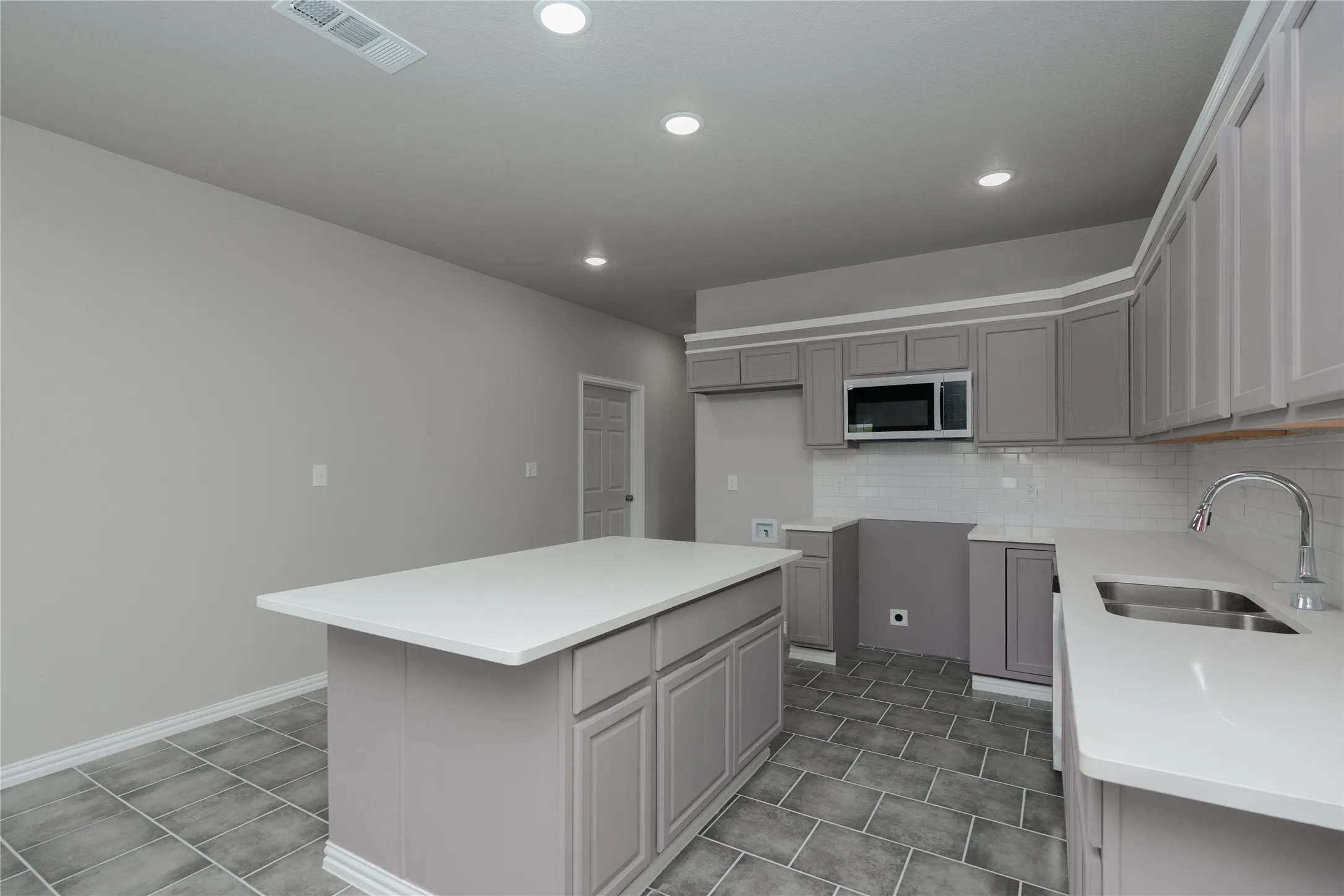 Kitchen featuring a central island with white countertop, recessed lighting, gray cabinetry, subway tile backsplash, and a double basin sink with a gooseneck faucet