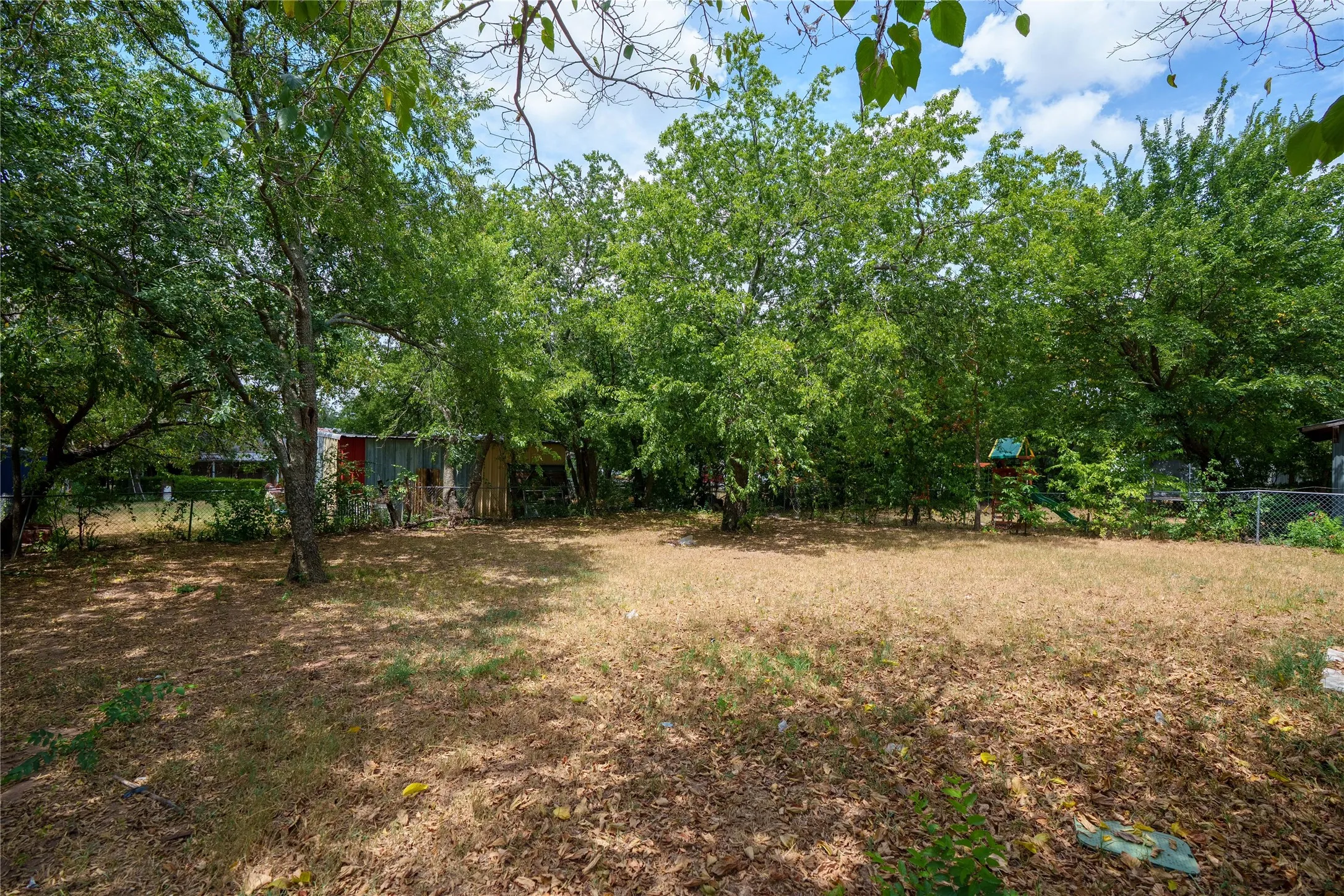 Expansive backyard area featuring mature trees and partial fencing