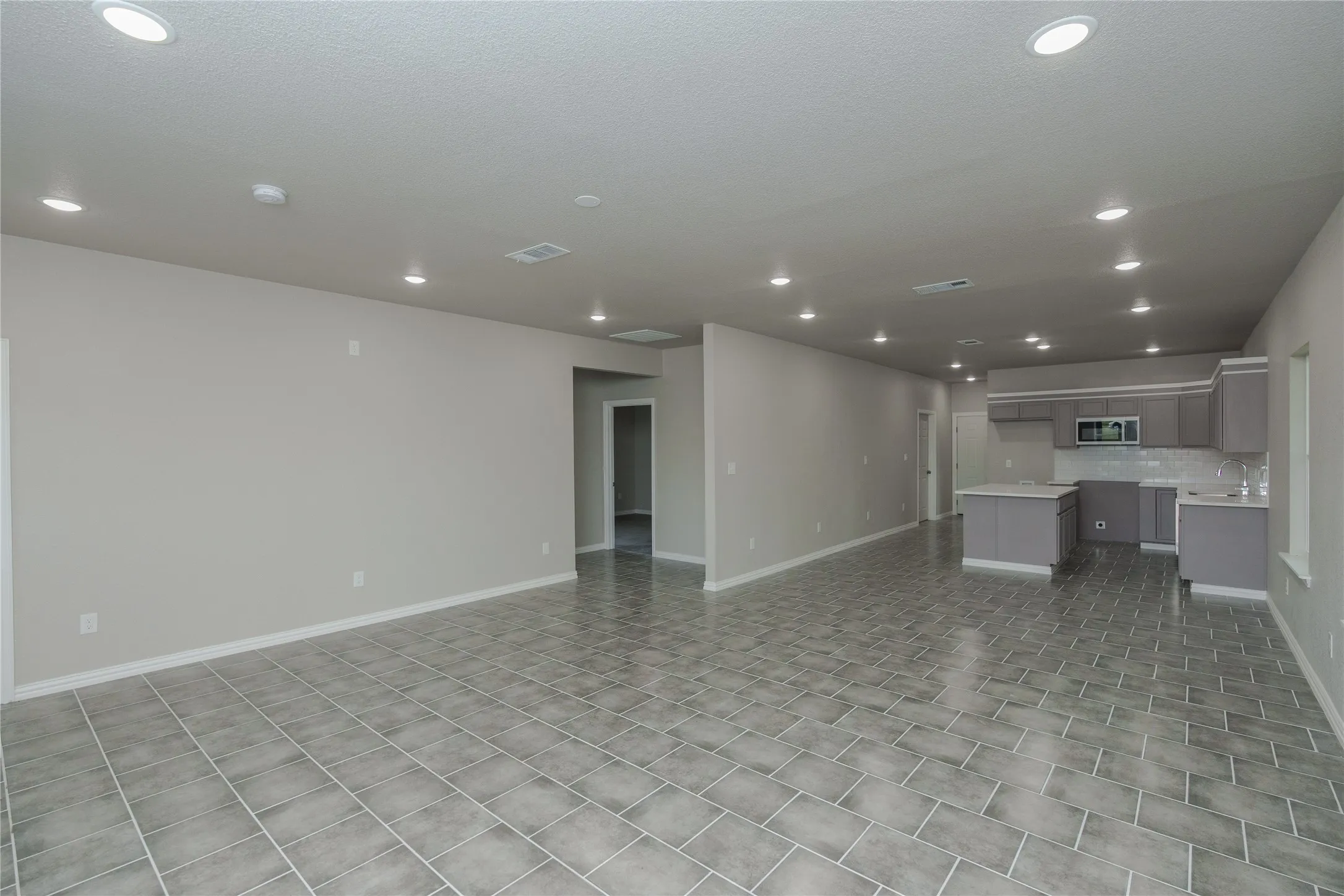 Spacious interior with gray tile flooring, recessed lighting, and a modern kitchen featuring gray cabinetry, a white countertop, and a subway tile backsplash