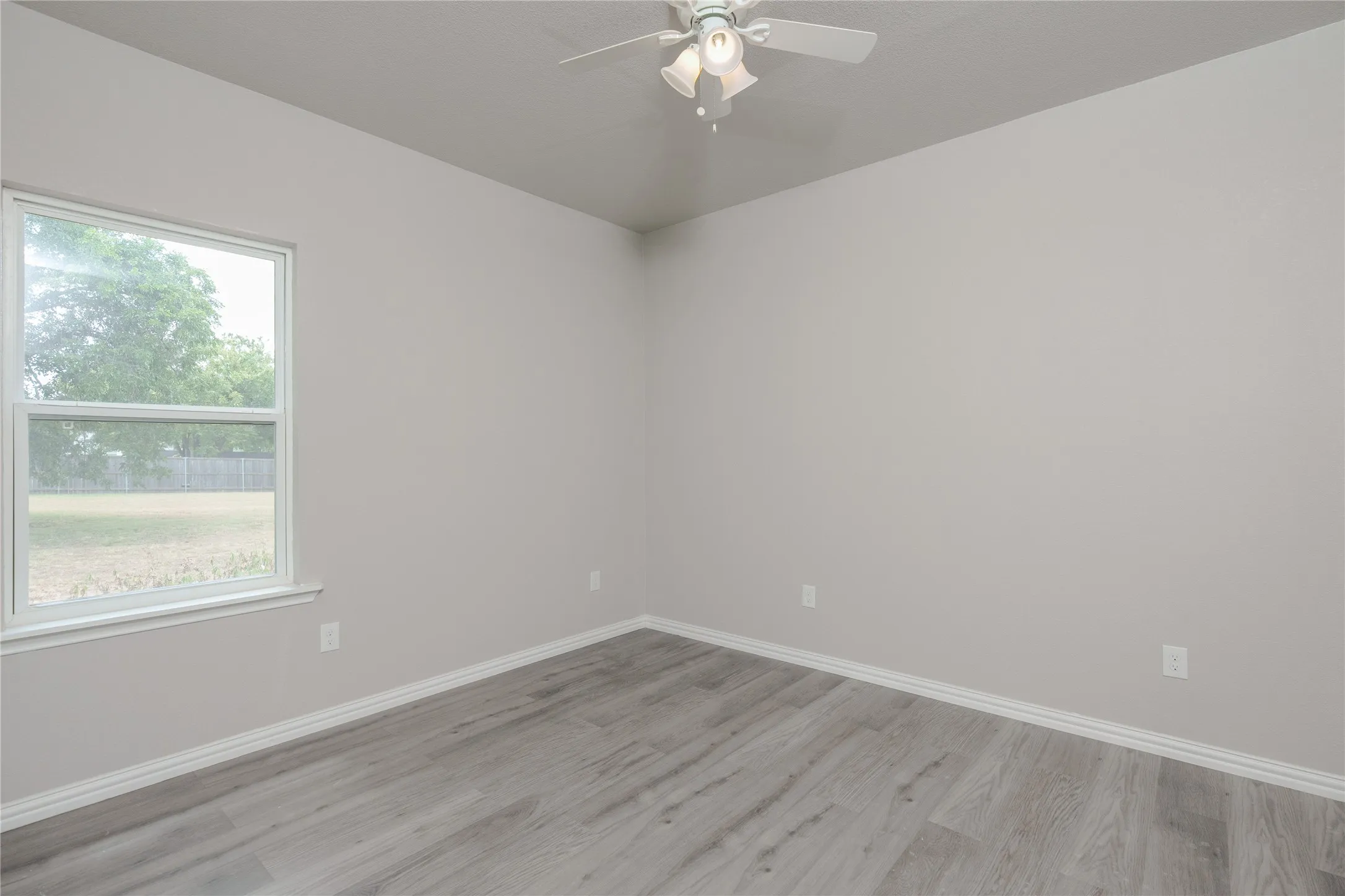 Room featuring light gray walls, wood-finish flooring, white baseboards, and a ceiling fan with integrated lighting