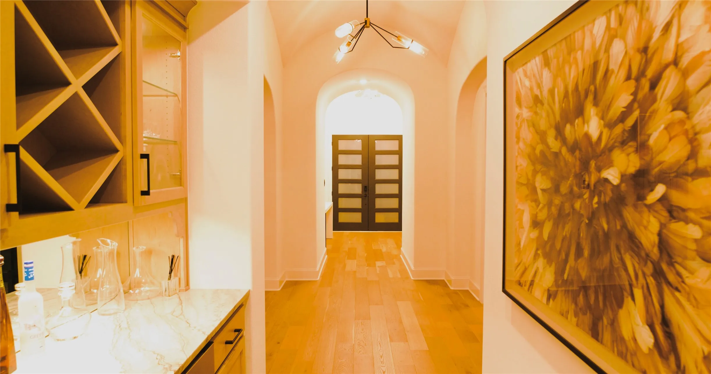 Hallway featuring light wood-finish flooring, arched doorways, a geometric chandelier, and built-in cabinetry with a wine rack and stone countertop