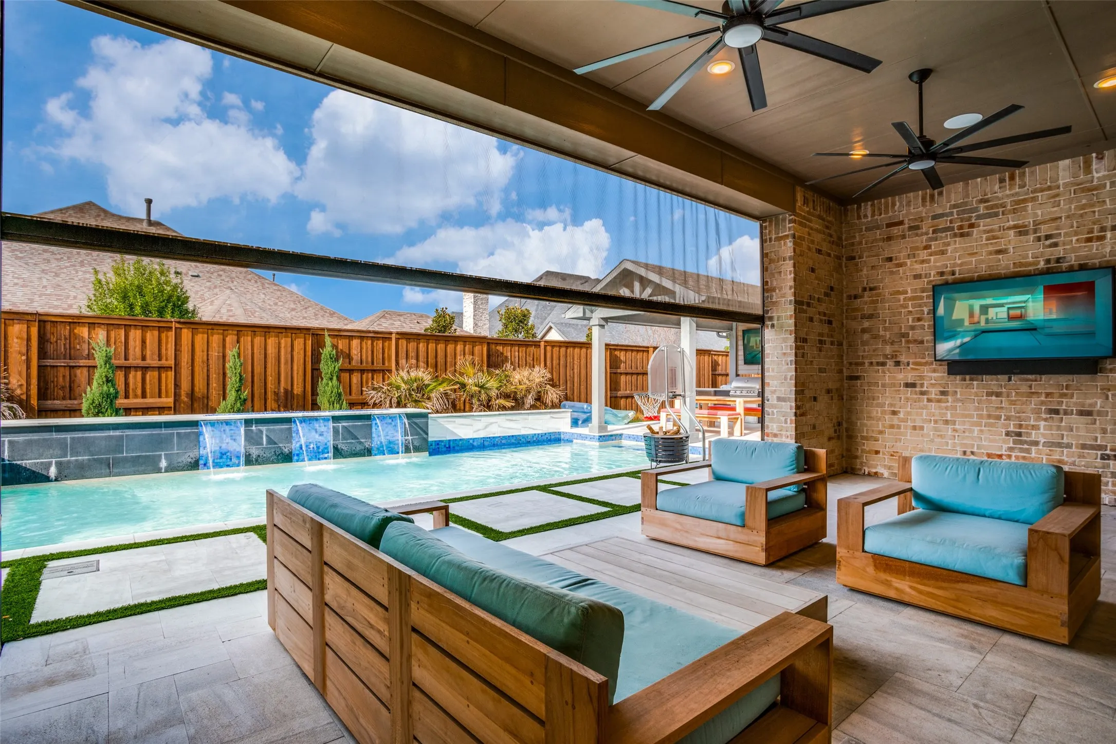 Covered outdoor living space featuring brick wall, ceiling fans, and a wall-mounted display