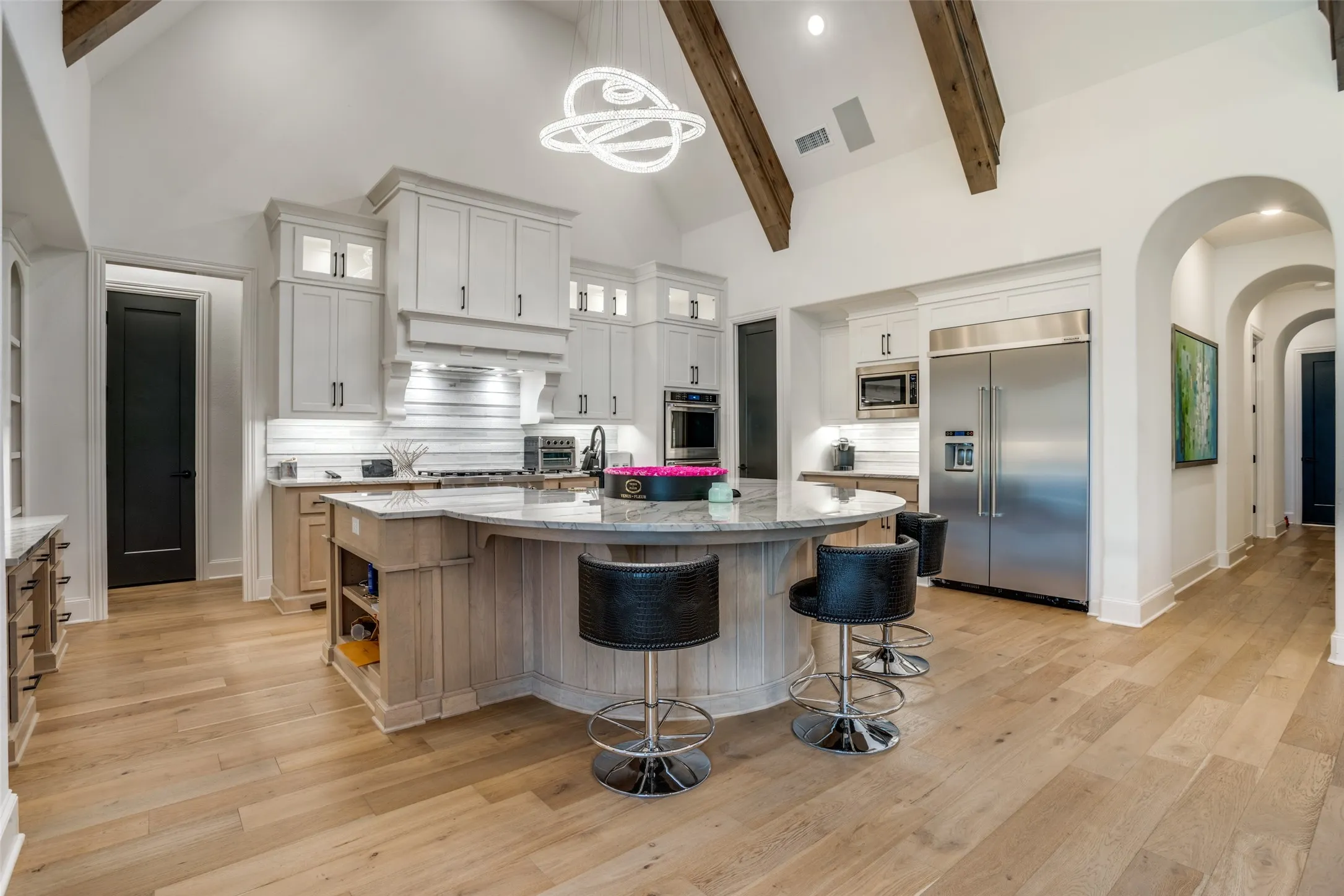 Kitchen featuring a curved central island with seating, a vaulted ceiling with exposed wood beams, and light wood-finish flooring