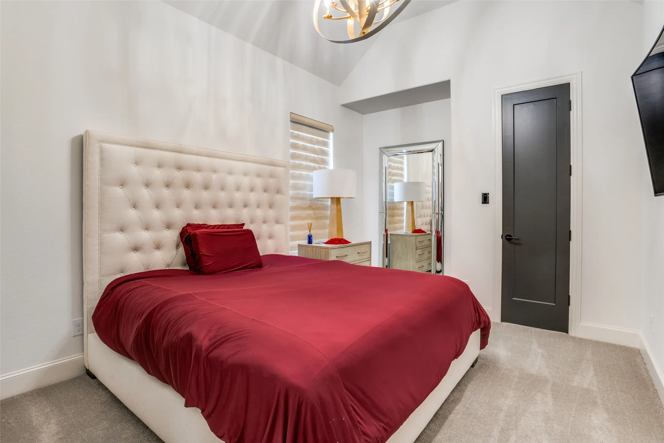 Vaulted ceiling with an overhead light fixture, light gray carpet, and a dark paneled door with black hardware