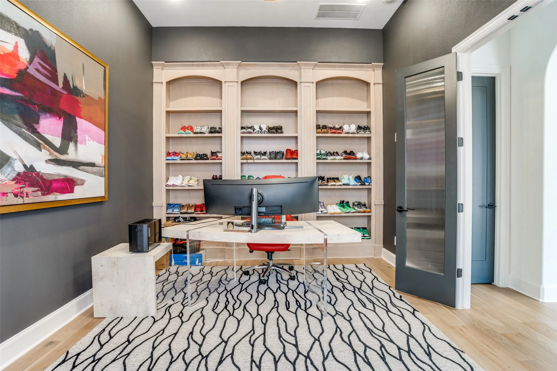 Integrated shelving unit with arched top sections and base cabinetry, light wood-finish flooring, and a modern door with reeded glass paneling