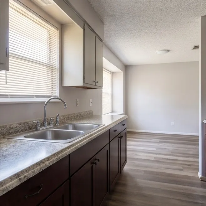 Kitchen featuring a double basin stainless steel sink, laminate countertops, dark wood-finish cabinetry, and light wood-finish flooring