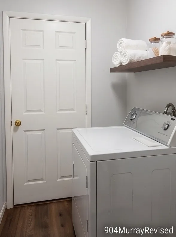 Wood-finish flooring with a white six-panel door, light gray walls, a floating wood-finish shelf, and a utility sink with a chrome faucet