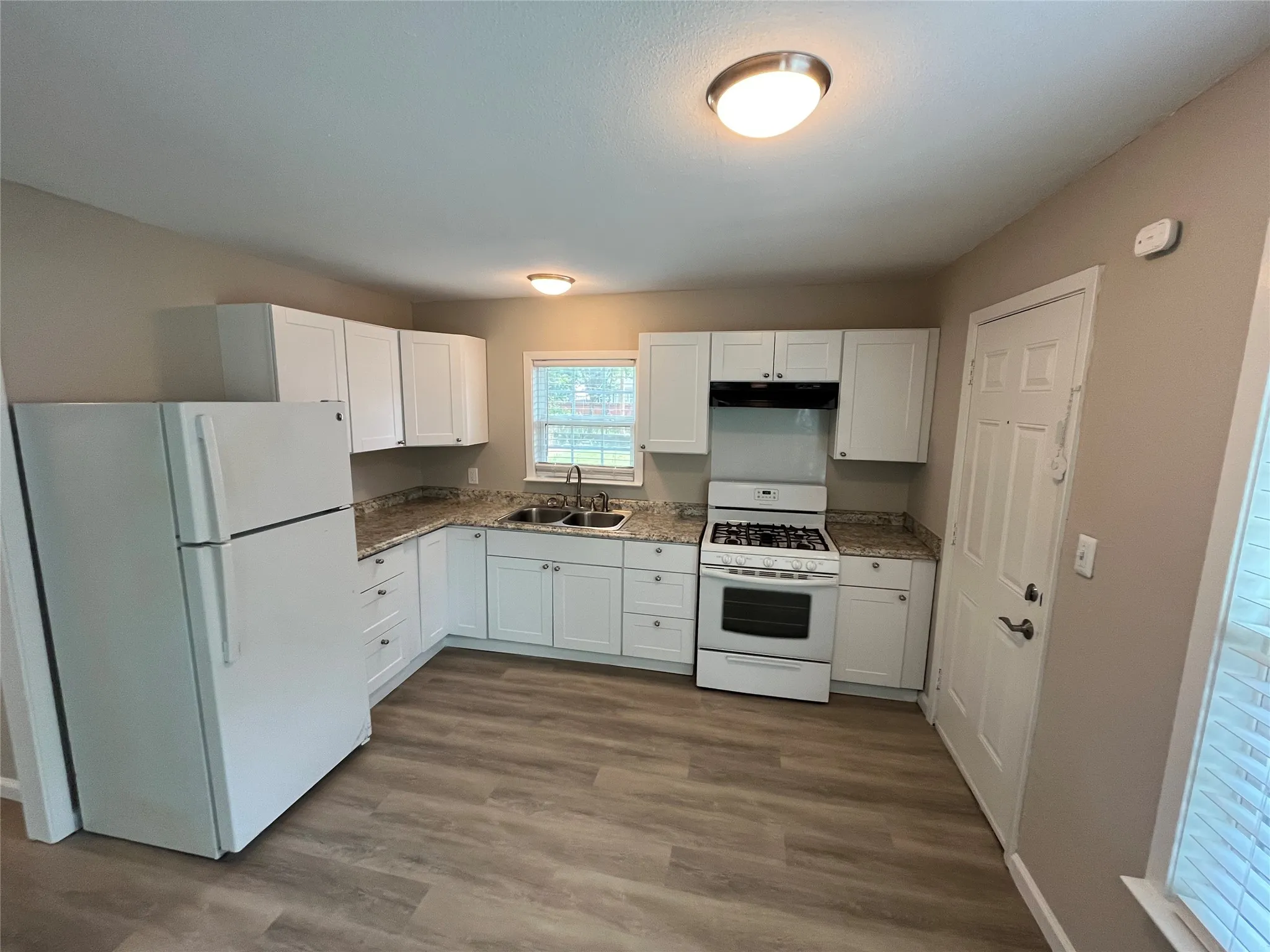 Kitchen featuring L-shaped cabinetry with white shaker-style doors, granite-look countertops, and wood-finish flooring