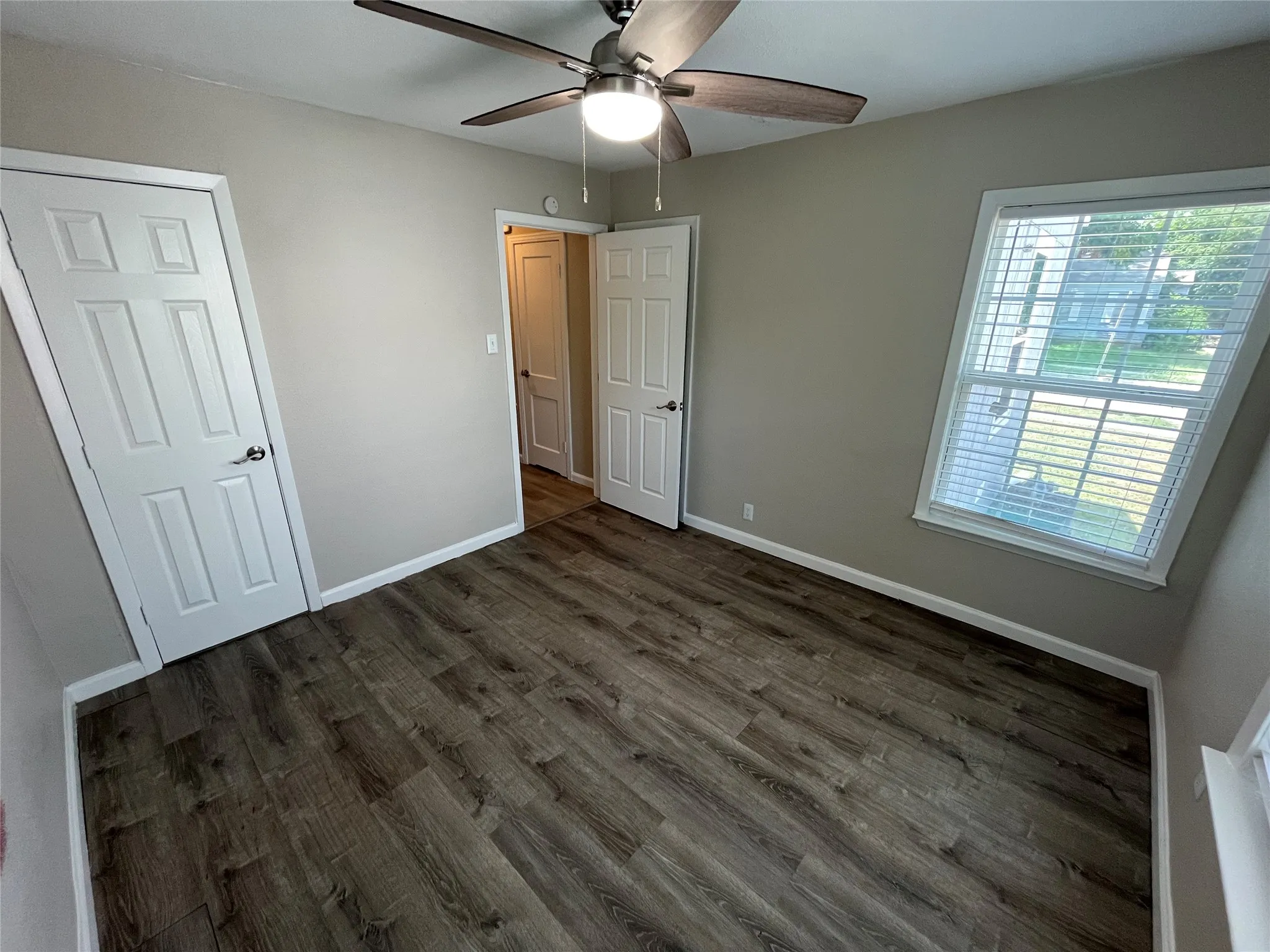 Spacious room featuring wood-finish flooring, neutral-toned walls, and a ceiling fan with integrated lighting