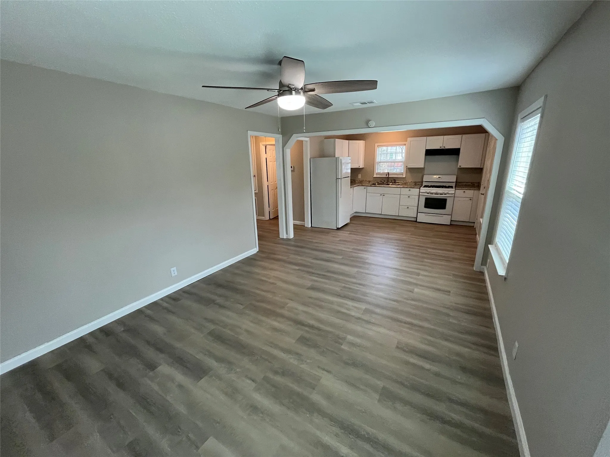 Open-concept living space featuring wood-finish flooring, a ceiling fan with integrated lighting, and neutral wall tones