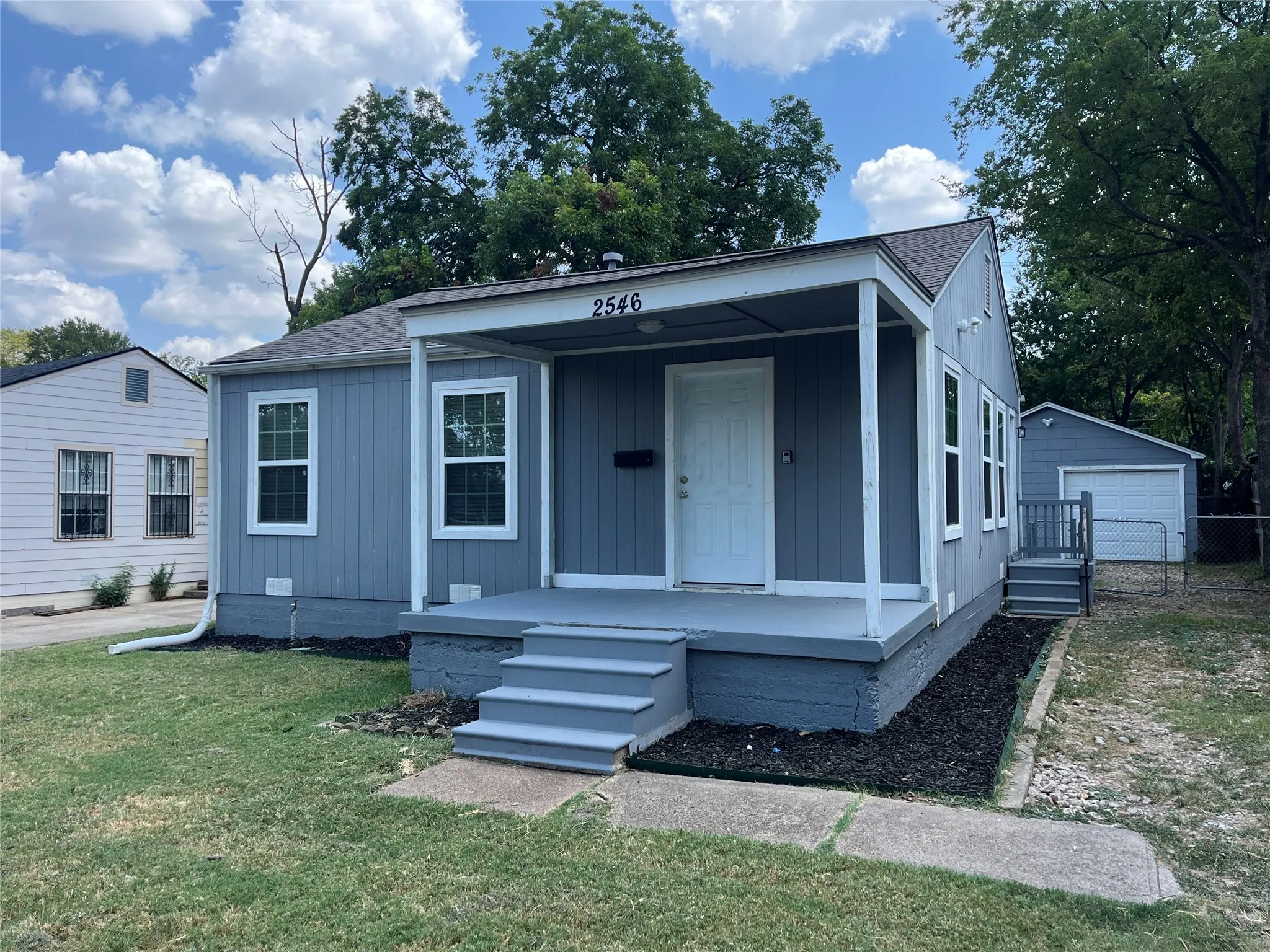 Exterior featuring gray siding, white trim windows, a covered front porch, and a detached gray garage with a white door
