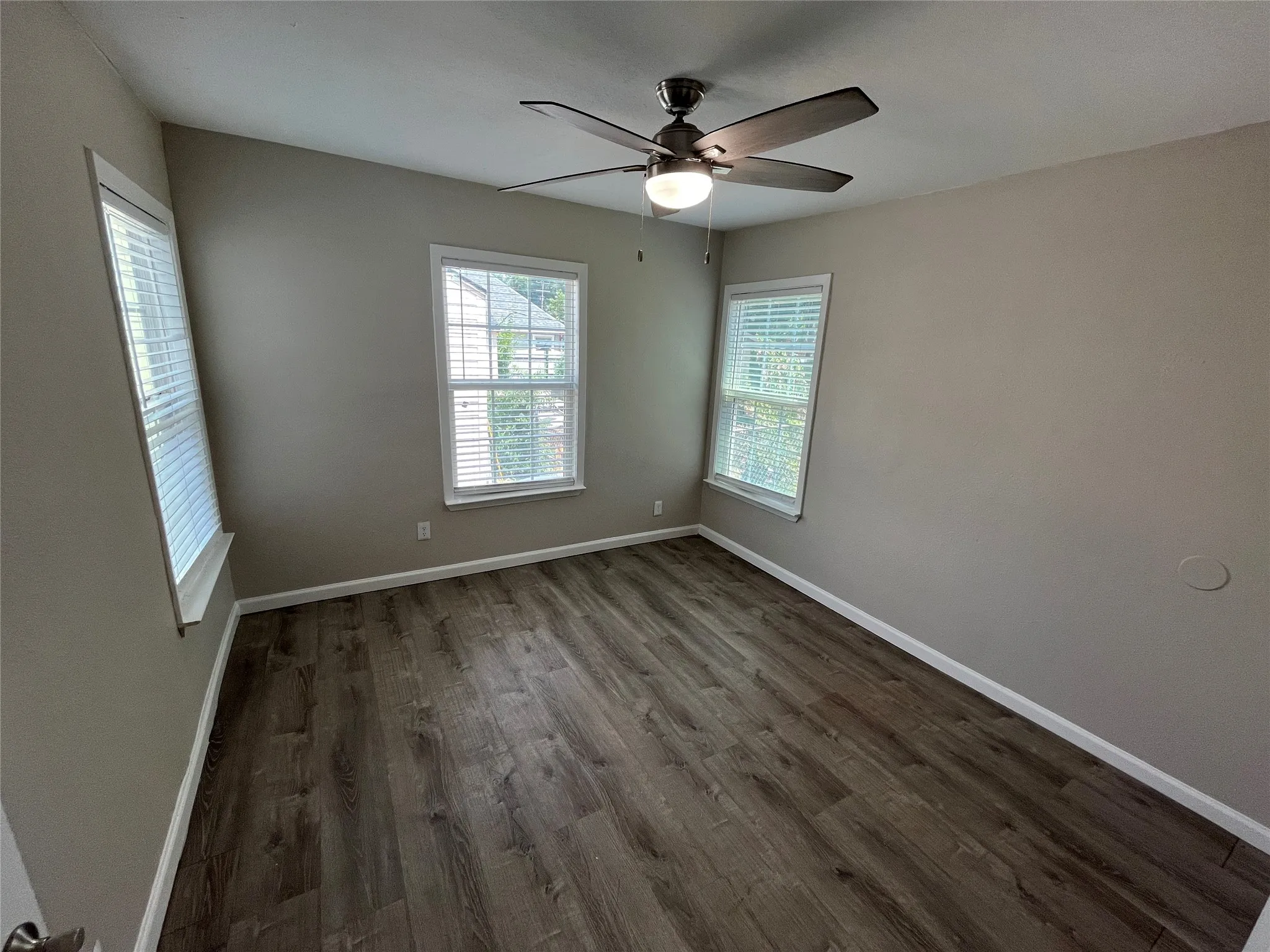 Interior room featuring wood-finish flooring, two windows with blinds, a ceiling fan with integrated lighting, and neutral wall paint