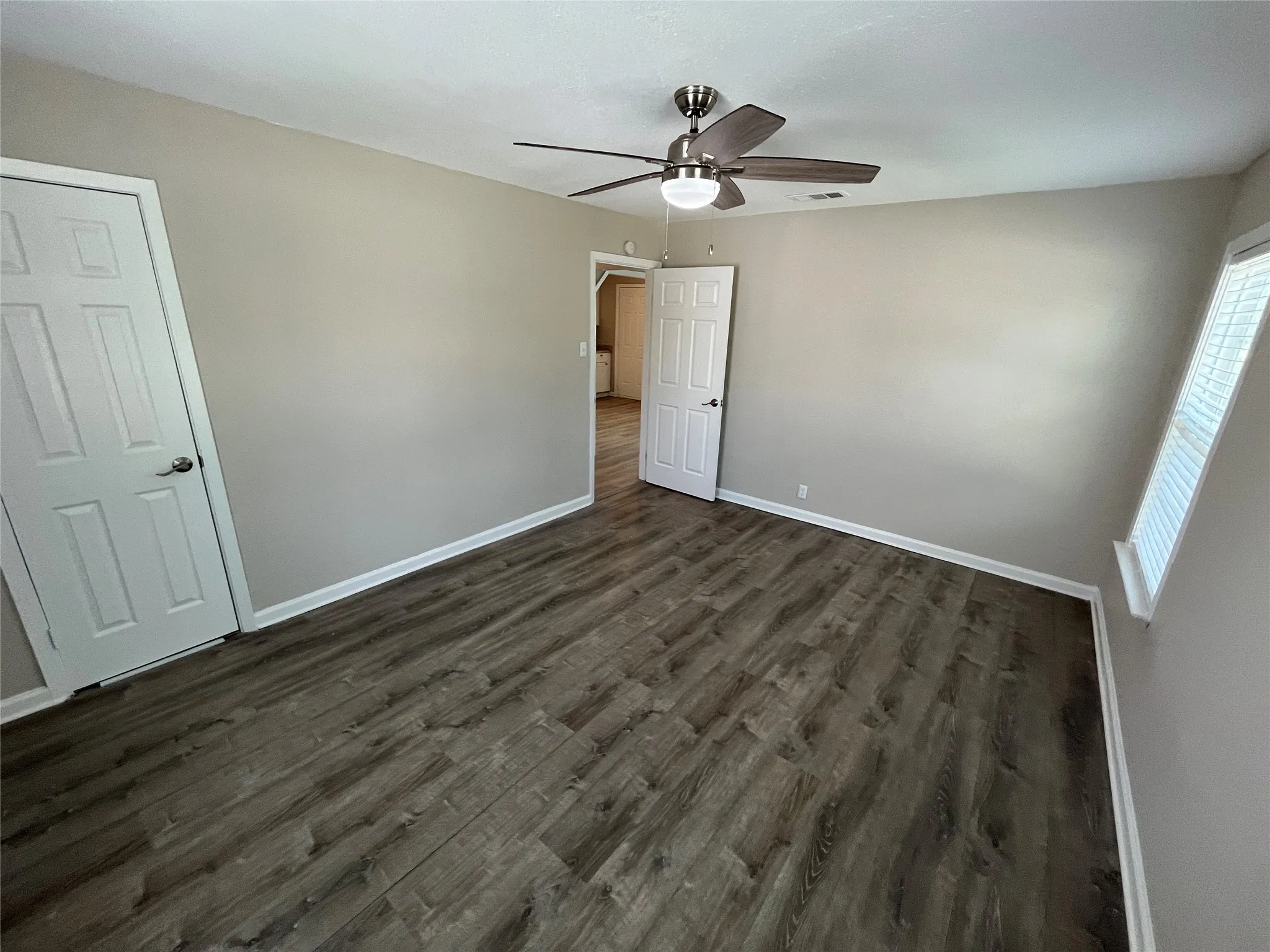 Spacious room featuring wood-finish flooring, neutral-toned walls, and white baseboards