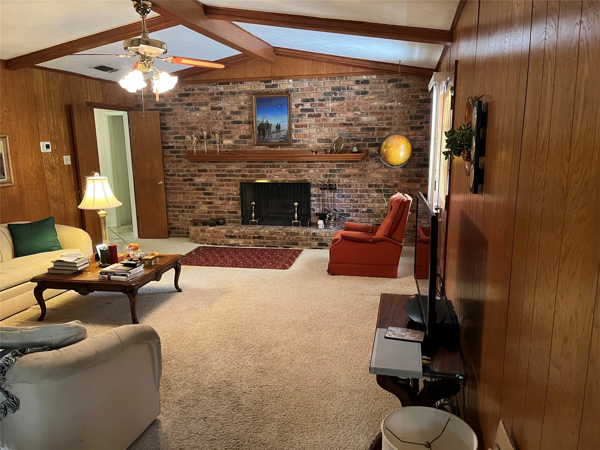 Living area featuring a brick fireplace with a wood mantle, wood-paneled walls, and a ceiling fan with integrated lighting