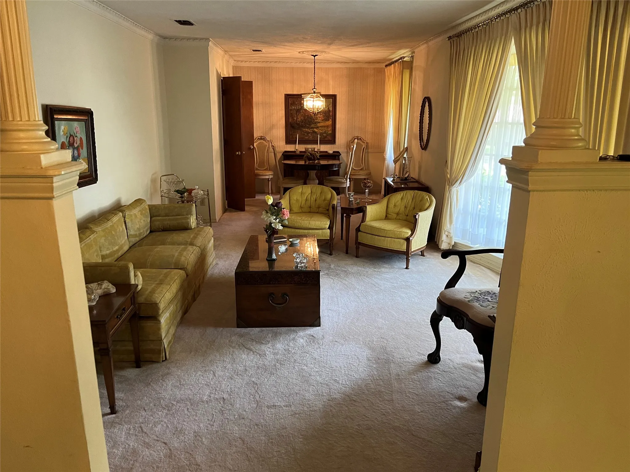 Spacious room featuring light-colored carpeting, decorative crown molding, and large windows with full-length draperies