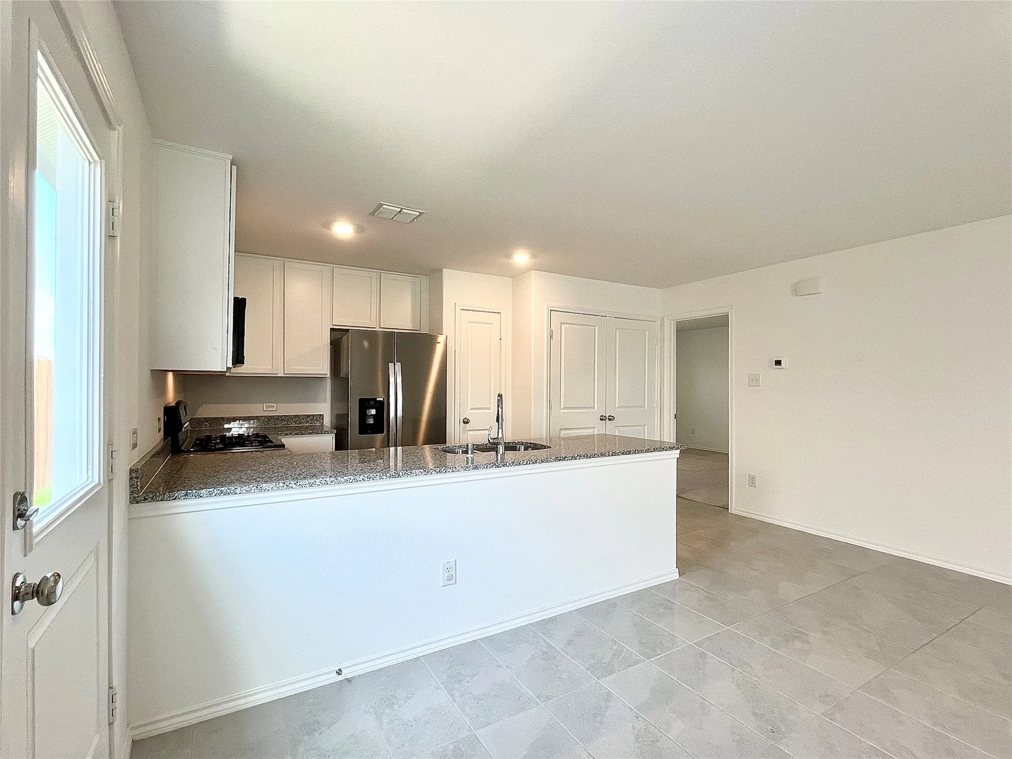 Kitchen with stainless steel fridge, a peninsula, stove, stone counters, and white cabinets