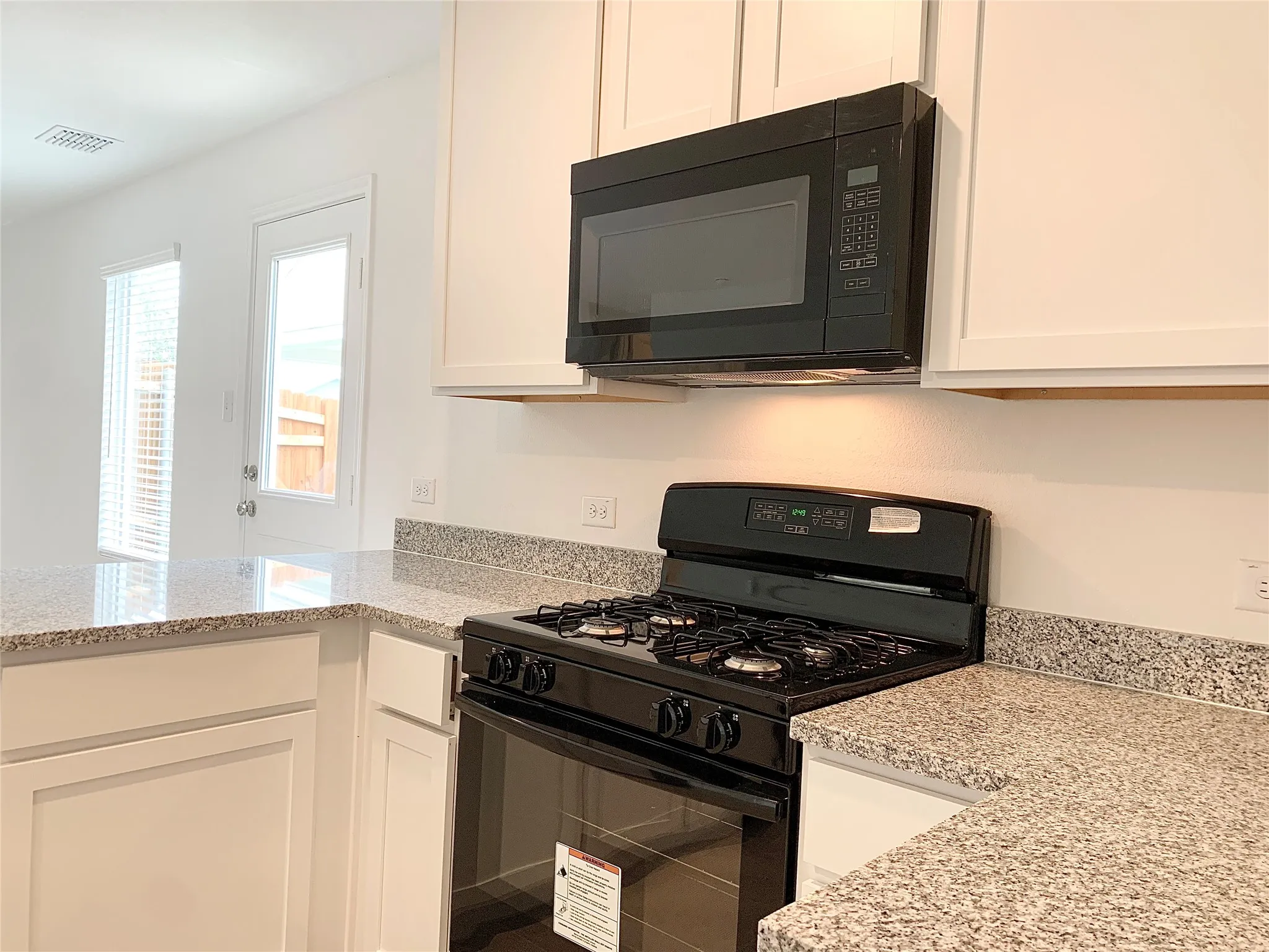 Kitchen with light stone counters, white cabinetry, and black appliances