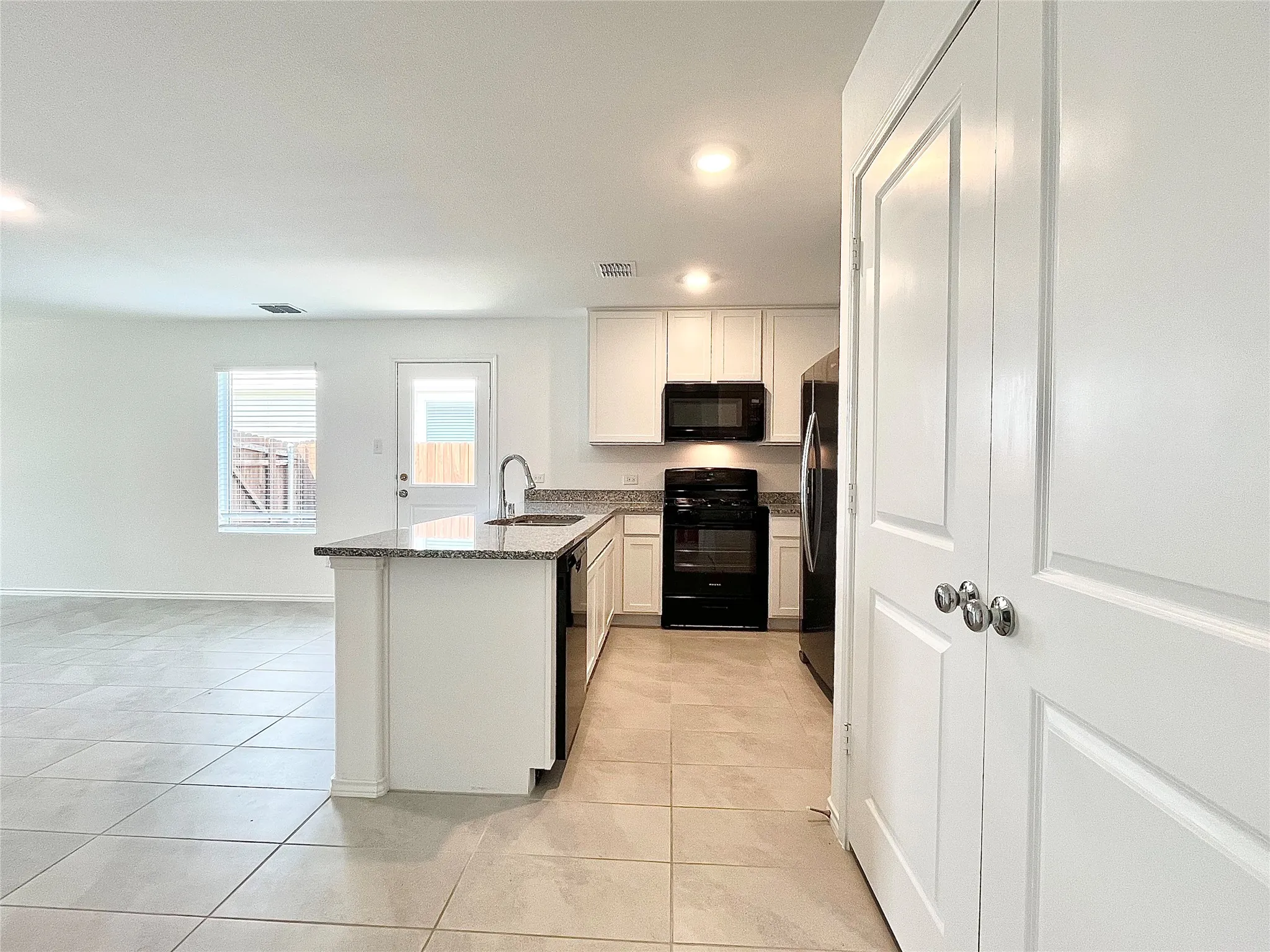 Kitchen featuring black appliances, a peninsula, stone counters, light tile patterned floors, and recessed lighting