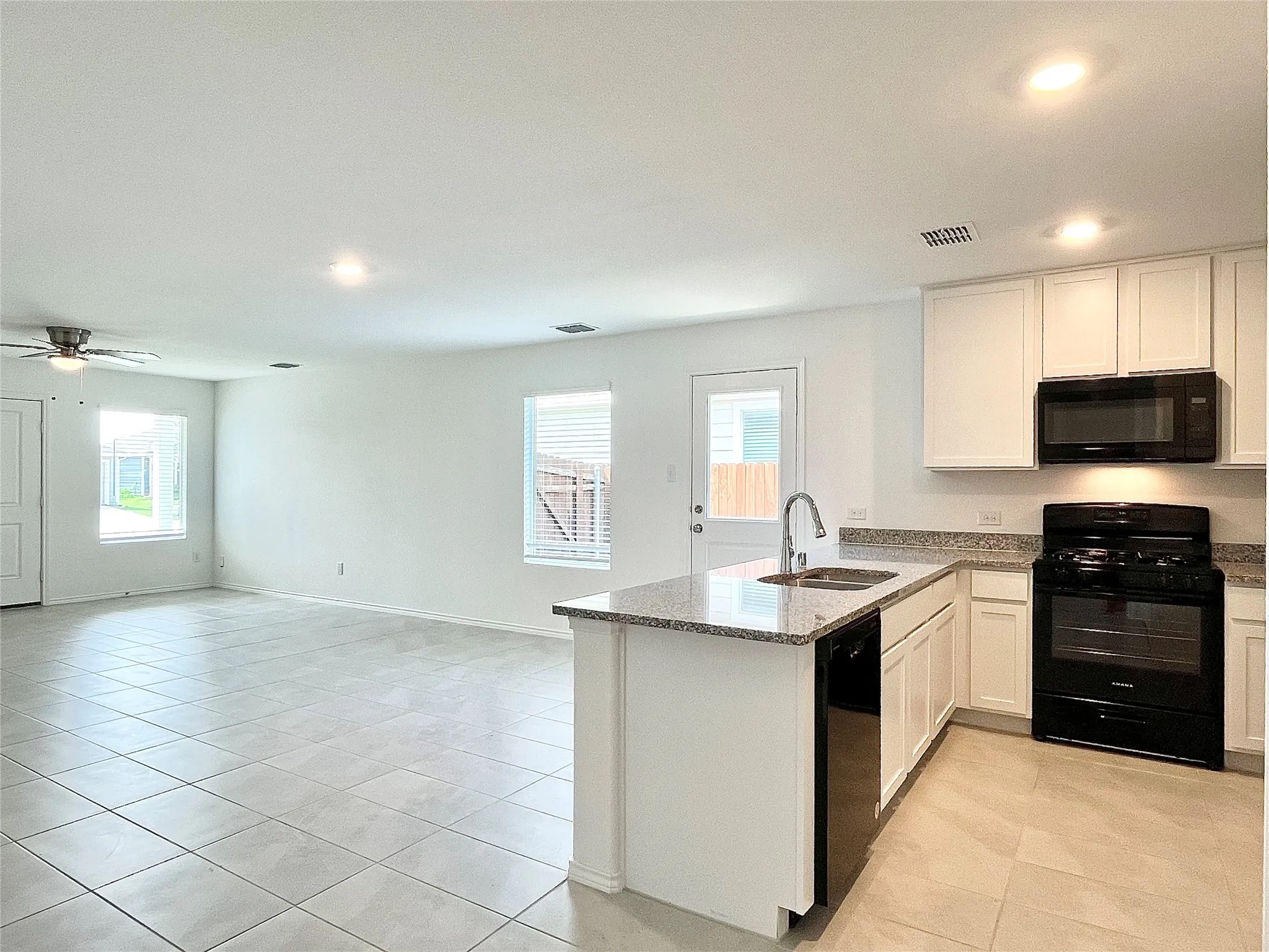 Kitchen with black appliances, a peninsula, open floor plan, light stone counters, and plenty of natural light